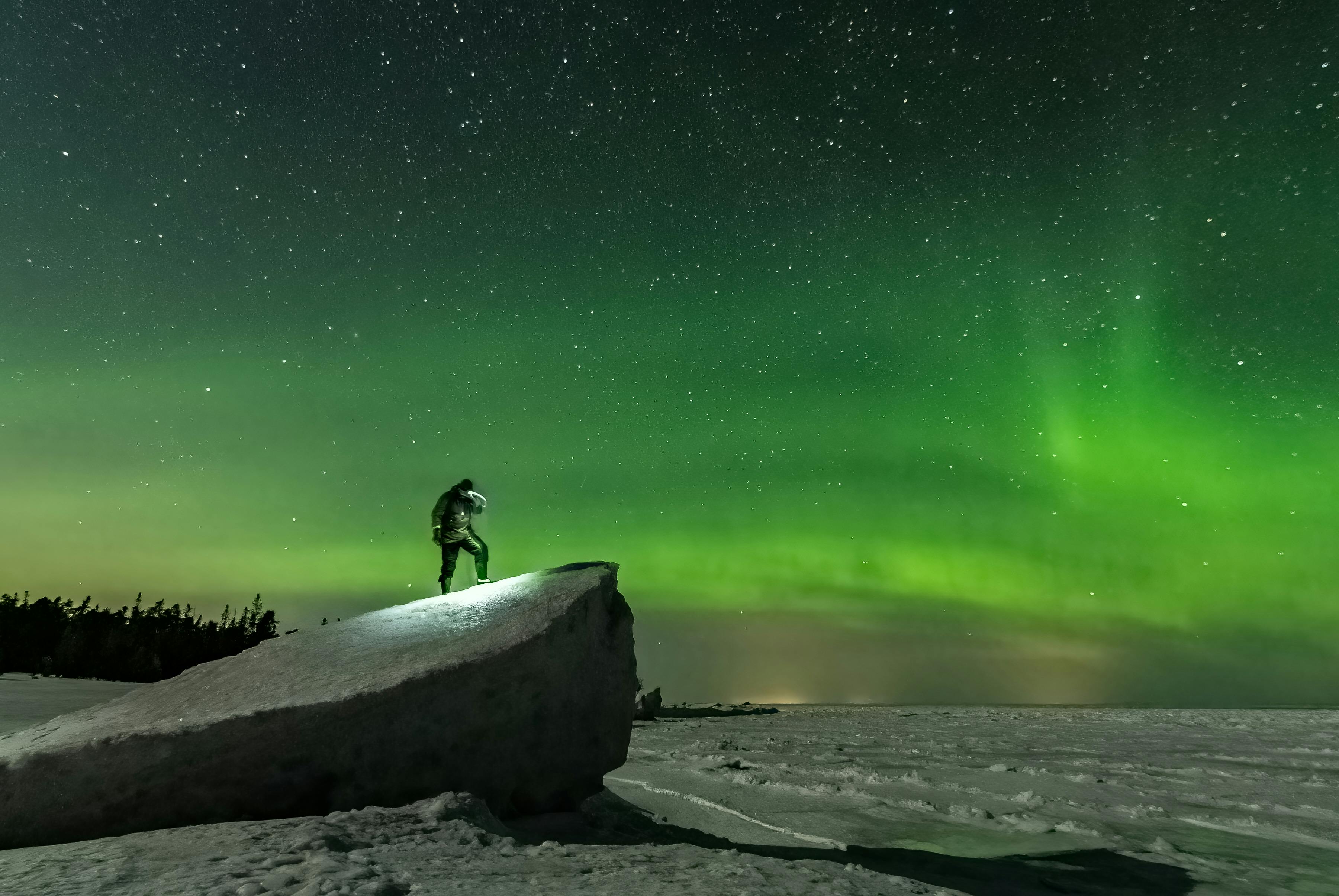 Badet i grønt Nordlys i Nordsverige med mand på sten