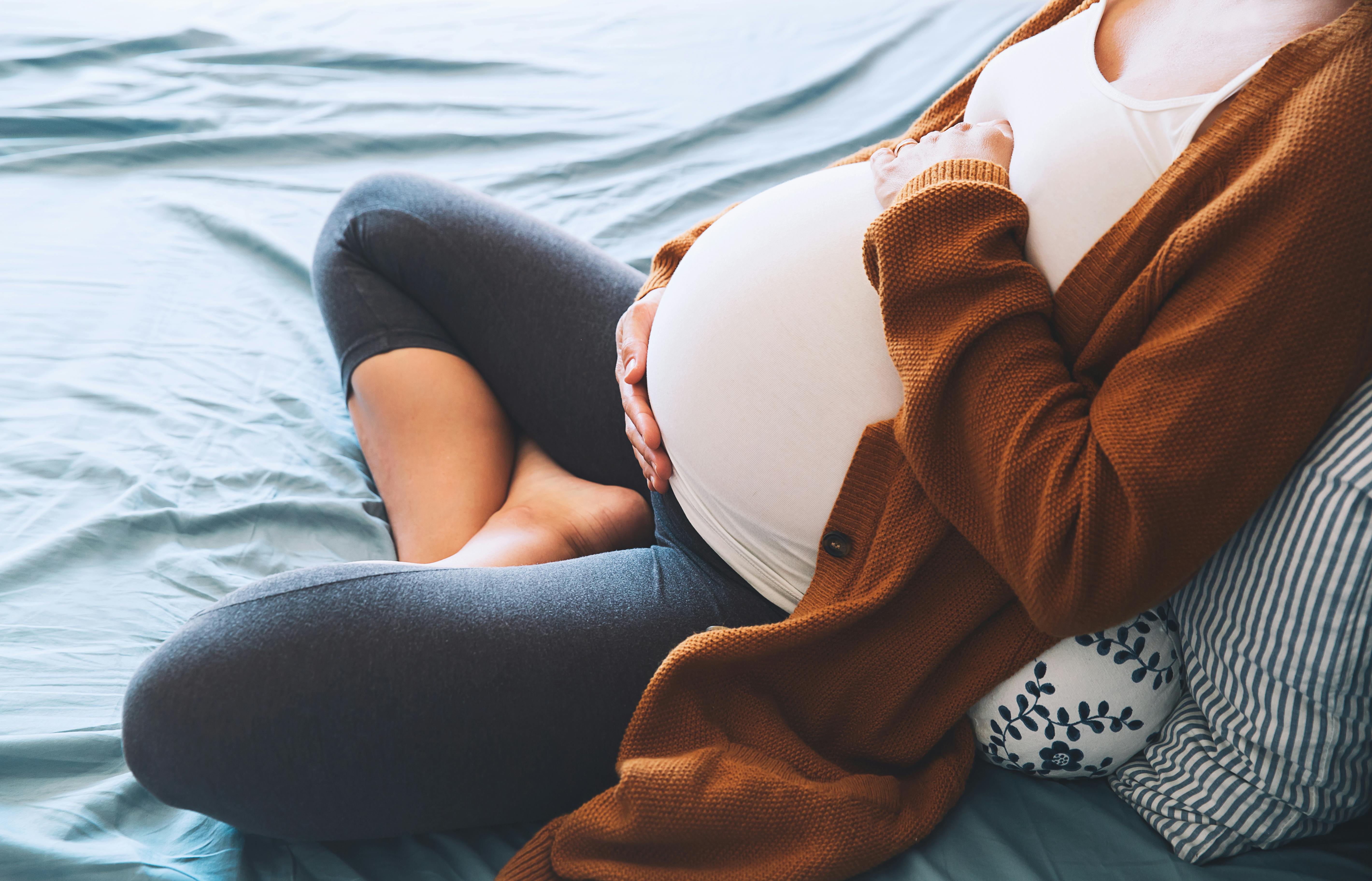 De fleste gravide føder i løbet af uge 40 af graviditeten. Kvinde, der er gravid i uge 40, sidder i sin seng og holder om sin mave