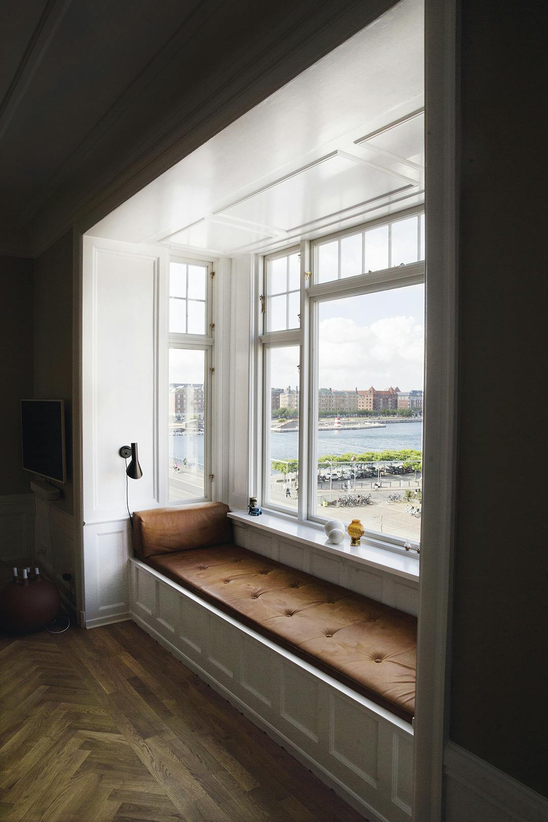 Het eerste wat Sif deed na de verhuizing, was een bank inbouwen in de erker, vanwaar je uitkijkt op het water aan de ene kant en het bruisende stadsleven aan de andere kant. Vensterbank in erker, met leren kussens en parketvloer.