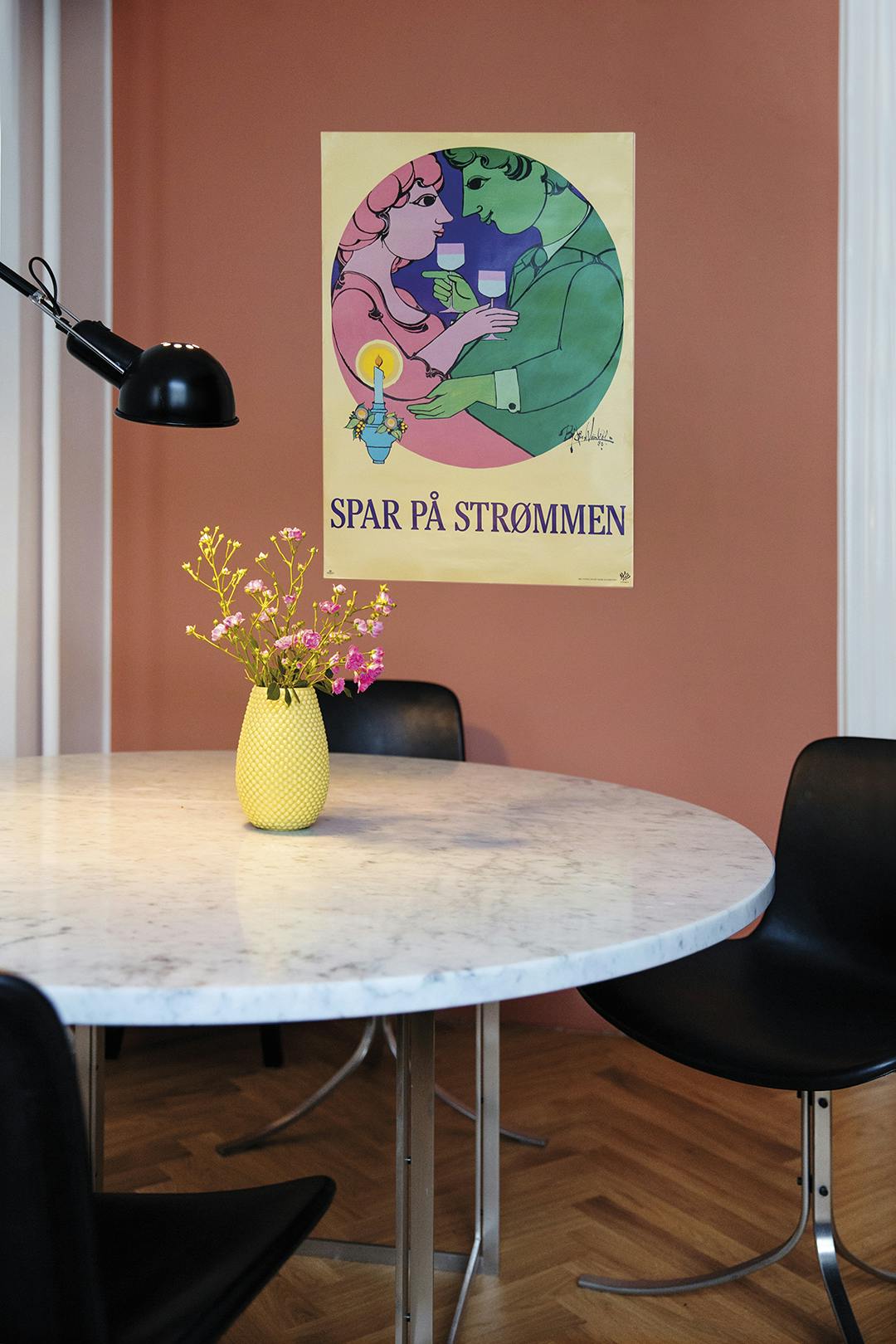 In de keuken hangt een oude poster van de kunstenaar Bjørn Wiinblad, die maant: ‘Bespaar elektriciteit’. De eettafel en stoelen zijn van Poul Kjærholm. Deense poster Bjørn Wiinblad, Poul Kjærholm stoelen en tafel.