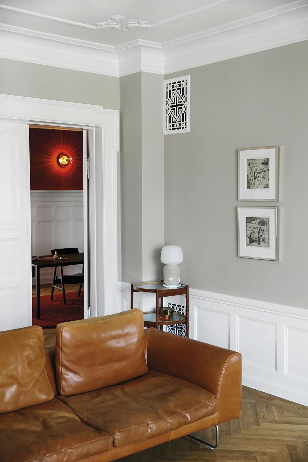 Op het ronde tafeltje staat een lamp/speaker, uit de serie Symfonisk die Ikea uitbracht in samenwerking met Sonos. Woonkamer met vintage leren bank en visgraat parketvloer.