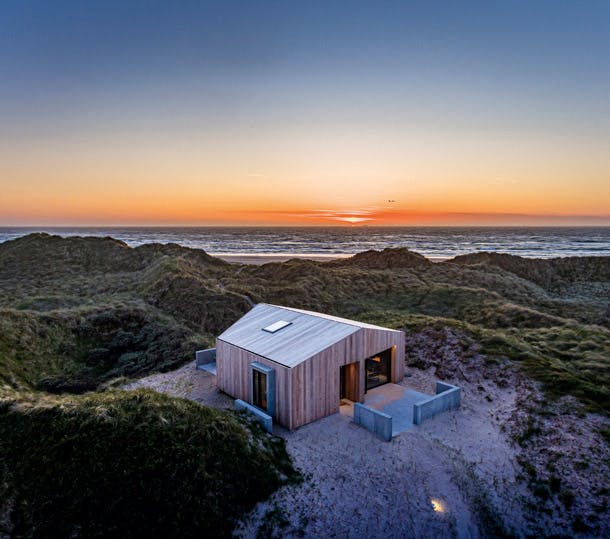 Het huis mocht niet hoger worden dan de omringende duinen. Nu is het klaar en het past perfect in de omgeving, met een prachtig uitzicht op de zonsondergang en de Noordzee. Het huis mocht niet hoger worden dan de omringende duinen. Nu is het klaar en het past perfect in de omgeving, met een prachtig uitzicht op de zonsondergang en de Noordzee.