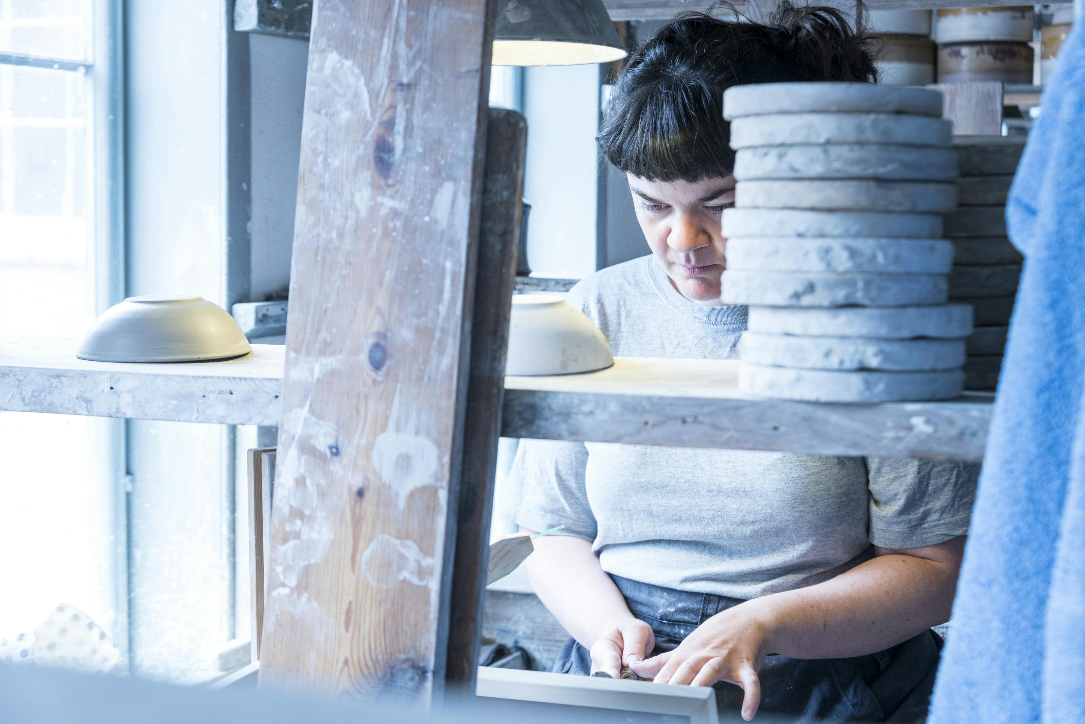 Professionel keramiker i arbejde på Hjorts Fabrik. Kvinde laver keramik og arbejder med ler.