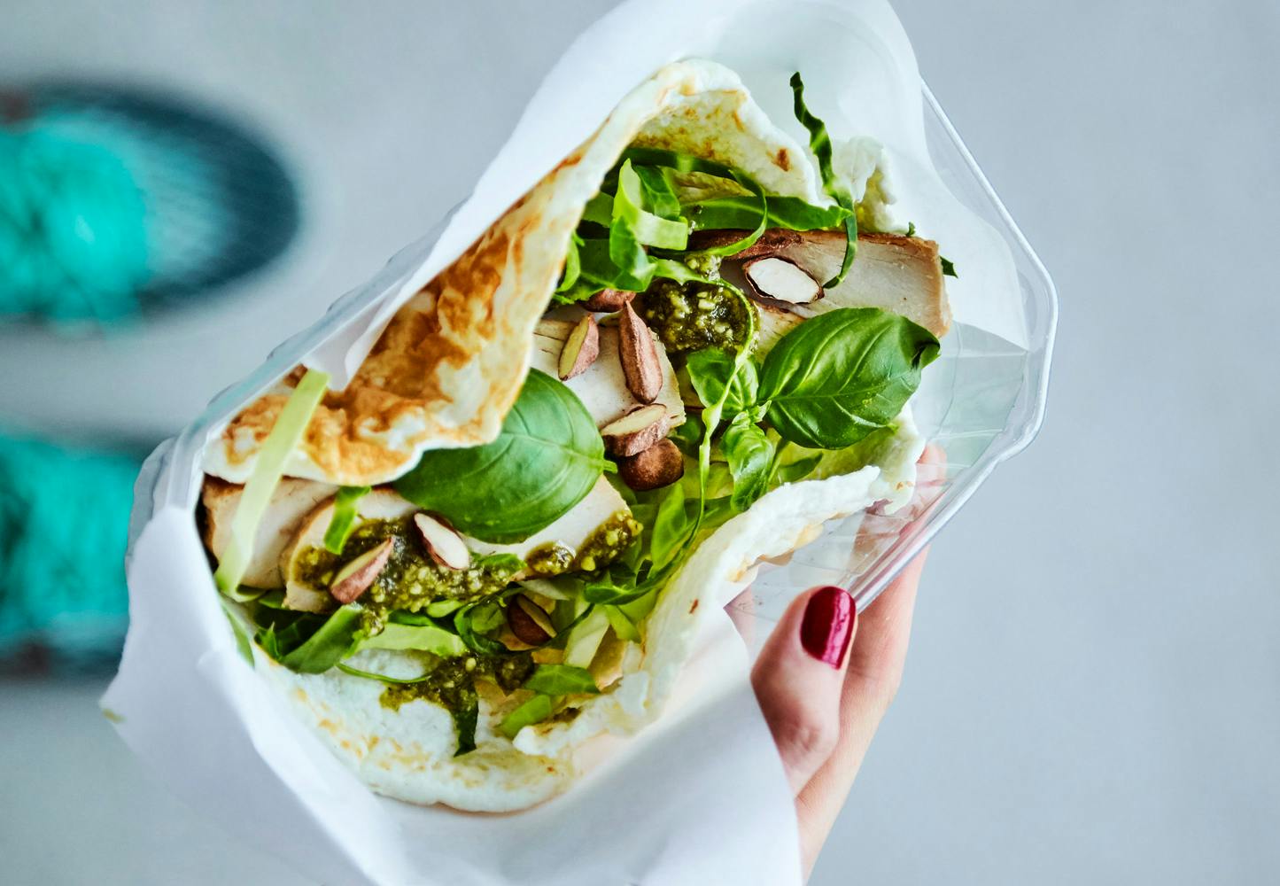 Kvinnehånd holder eggehvitewrap med kylling, spisskål, pesto og nøtter