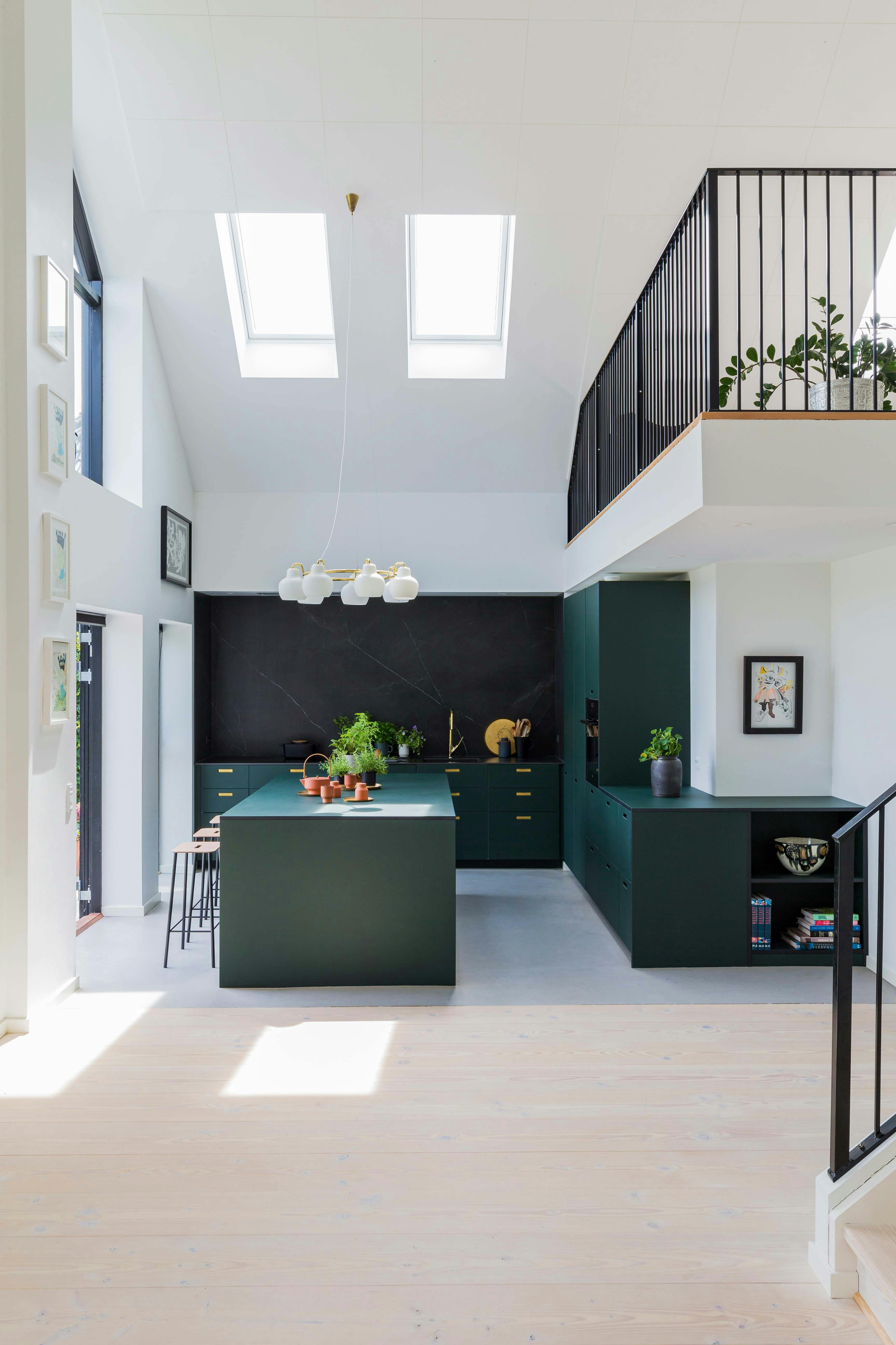 De keuken is van &Shufl. De vintage kroonluchter aan het plafond is van Vilhelm Lauritzen. andshufl linoleum keuken in groen met hoog plafond en vide