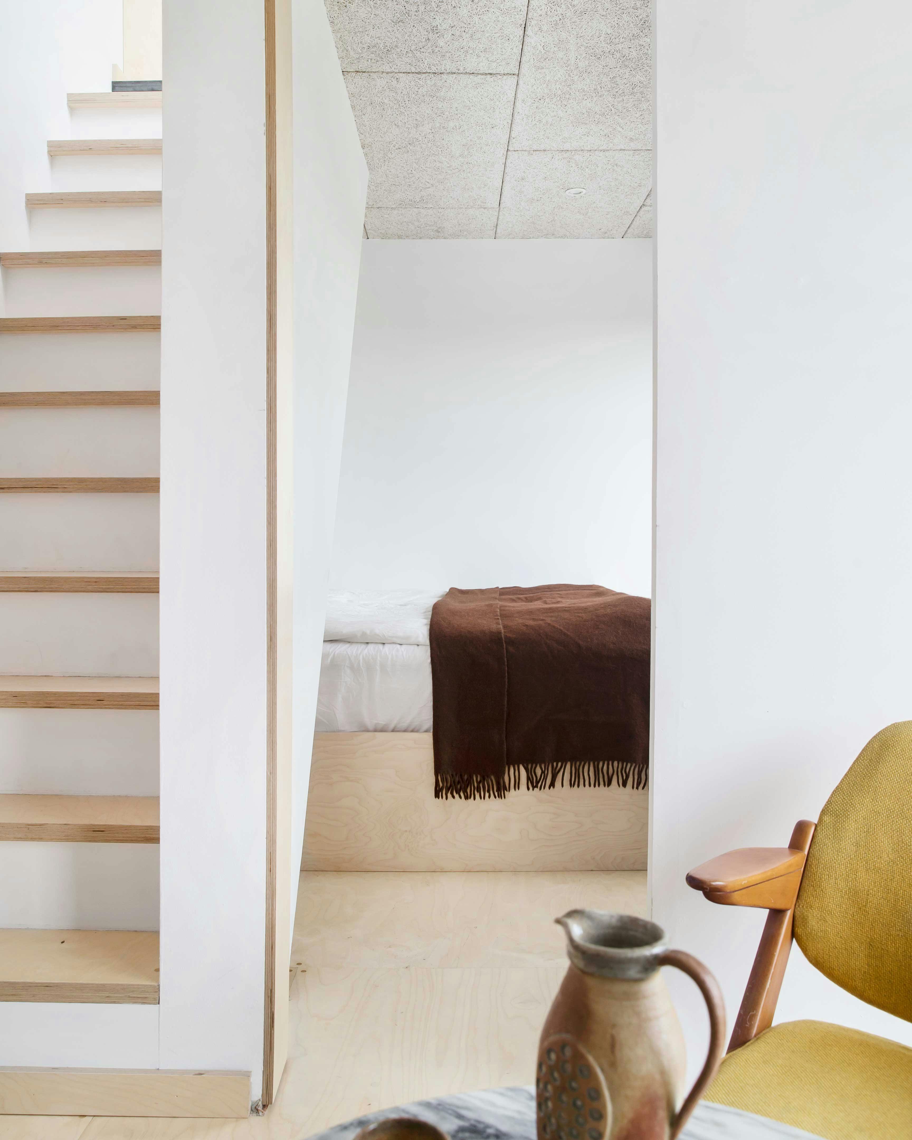 De slaapkamer grenst aan de woonkamer op de tweede verdieping. De trap leidt naar het dakterras. Spaanplaten bed en vloer lichte muren