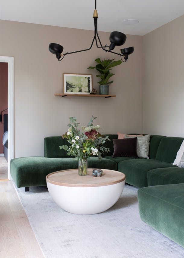 De donkergroene bank en de licht beige tint van Jotun (Sand1140) geven een knusse sfeer in de woonkamer. woonkamer met donkergroene bank en beige muur