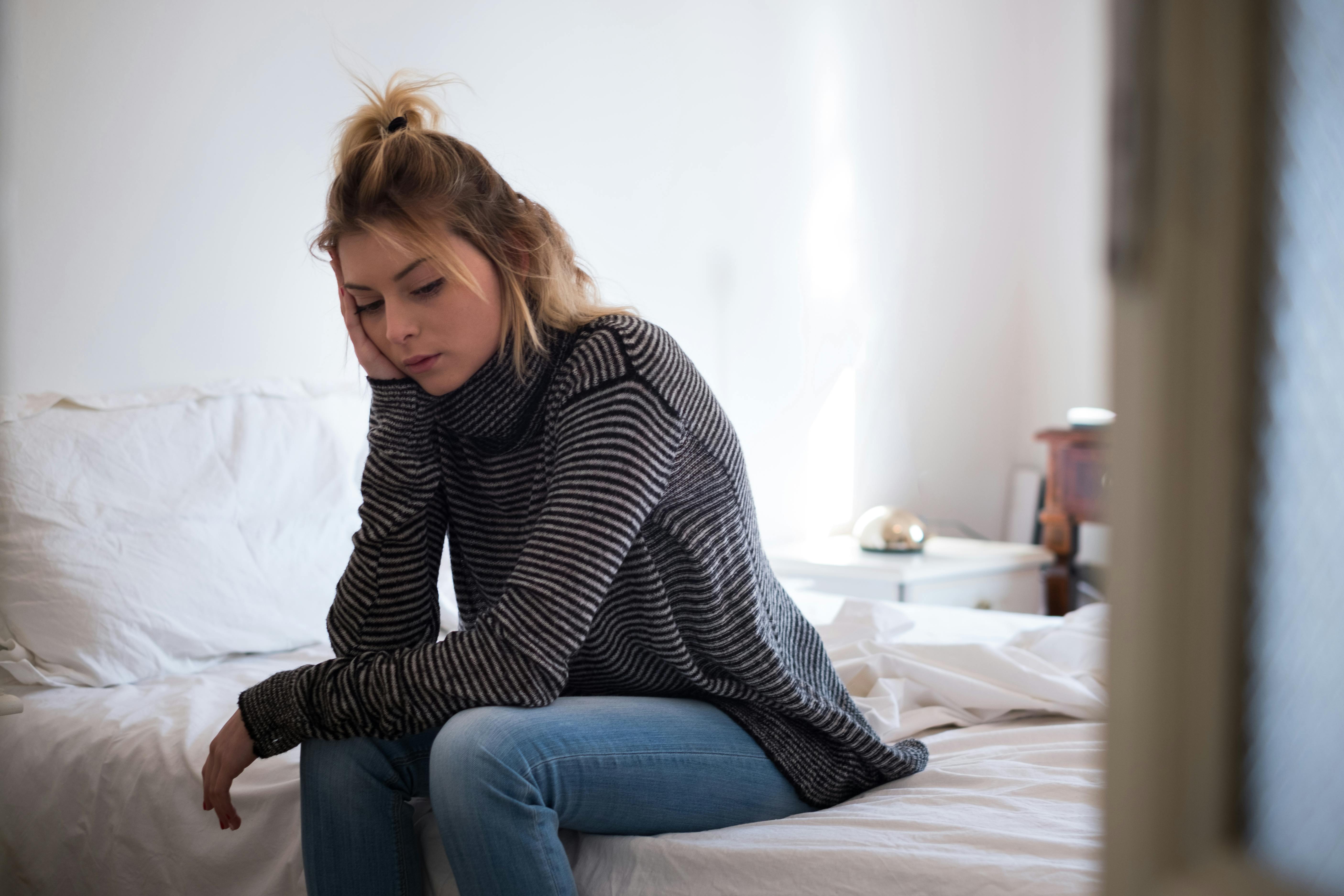 Hvis du er det sorte får, føler du sikkert, at du ikke kan leve op til din families forventninger. En kvinde sidder på en seng og ser trist ud