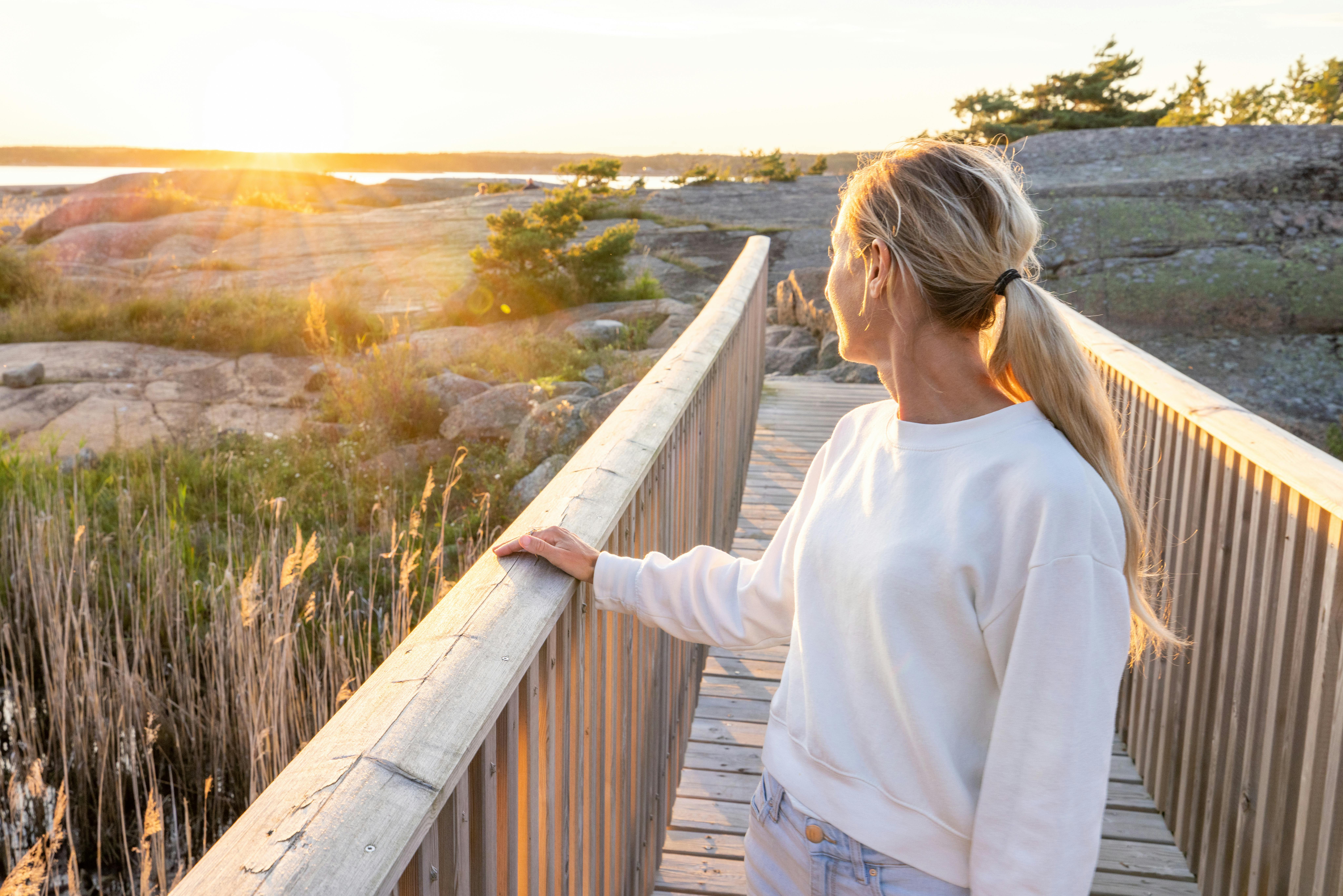 Som gravid i uge 13 begynder du måske at nyde graviditeten noget mere. Kvinde gravid i uge 13 står på en bro og kigger mod solen