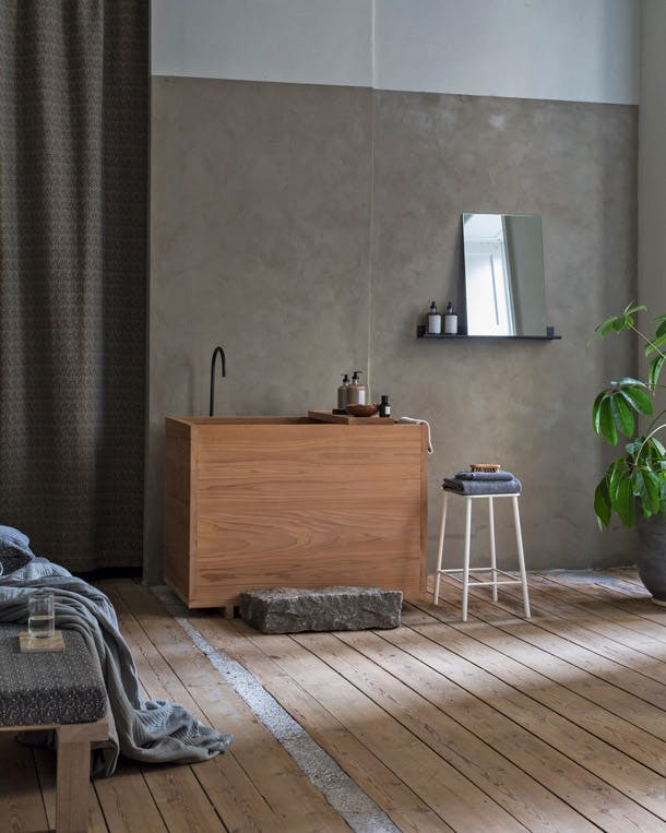 Het cederhouten bad is geïnspireerd op Japanse traditie. Het hout geeft aromatische geuren af als het nat wordt. Japans houten bad in scandinavische badkamer met ruwe vloer