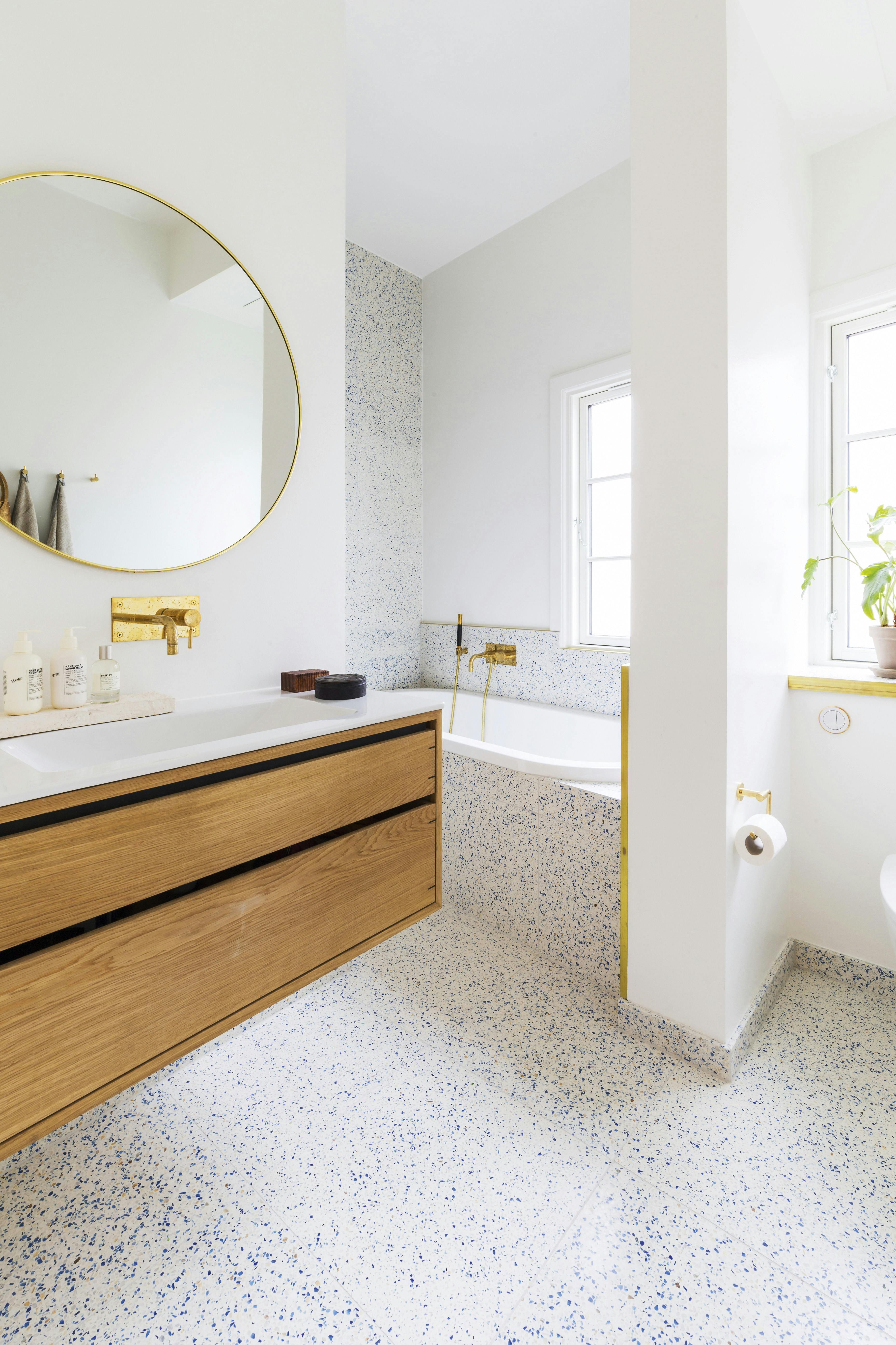 De messing accenten breken de lichte vlakken precies goed op. Terrazzo badkamer met ligbad en messing kranen