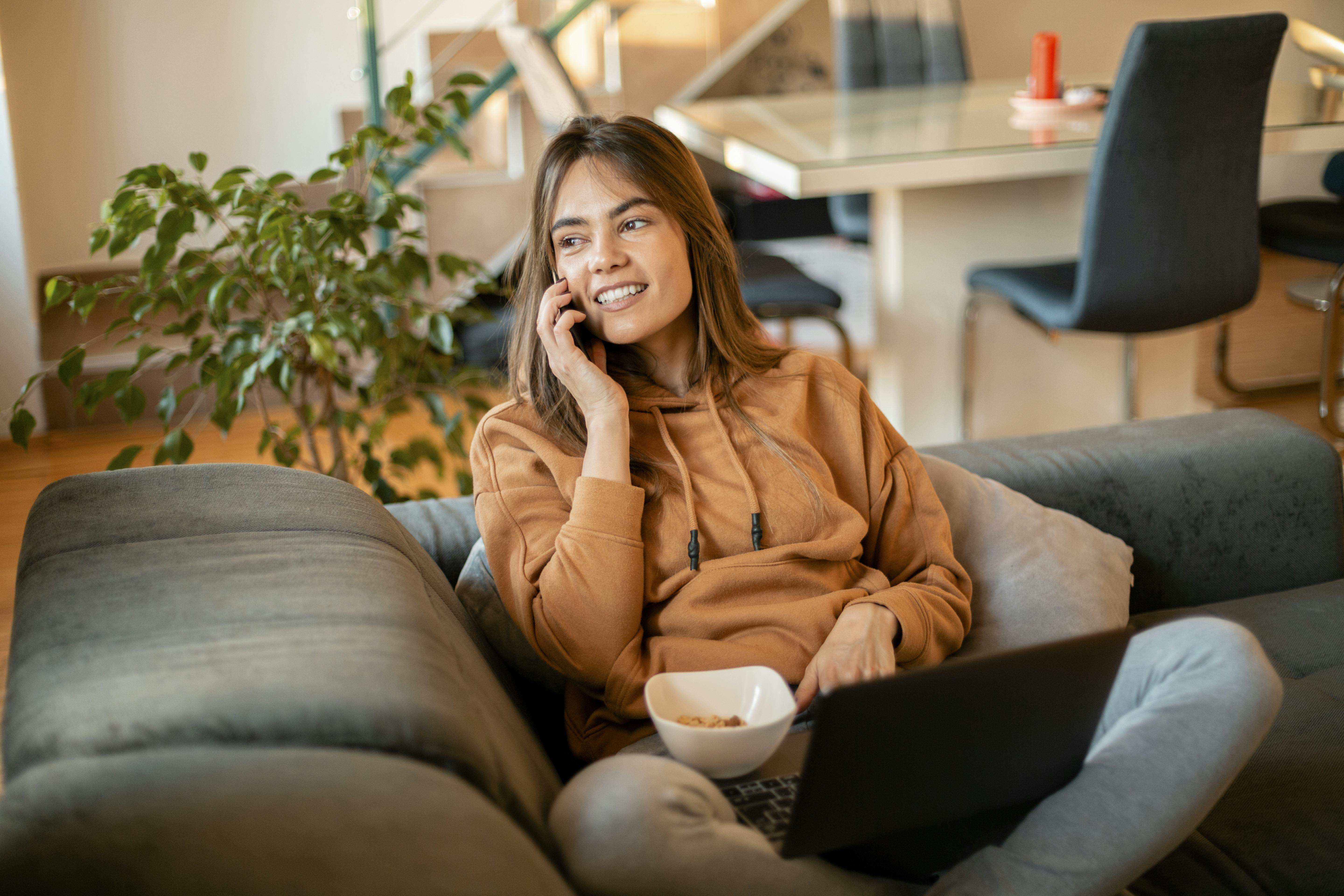 En telefonsamtale er også en god måde at dække noget af det sociale behov. Kvinde sidder med computer på sofa og taler i telefon