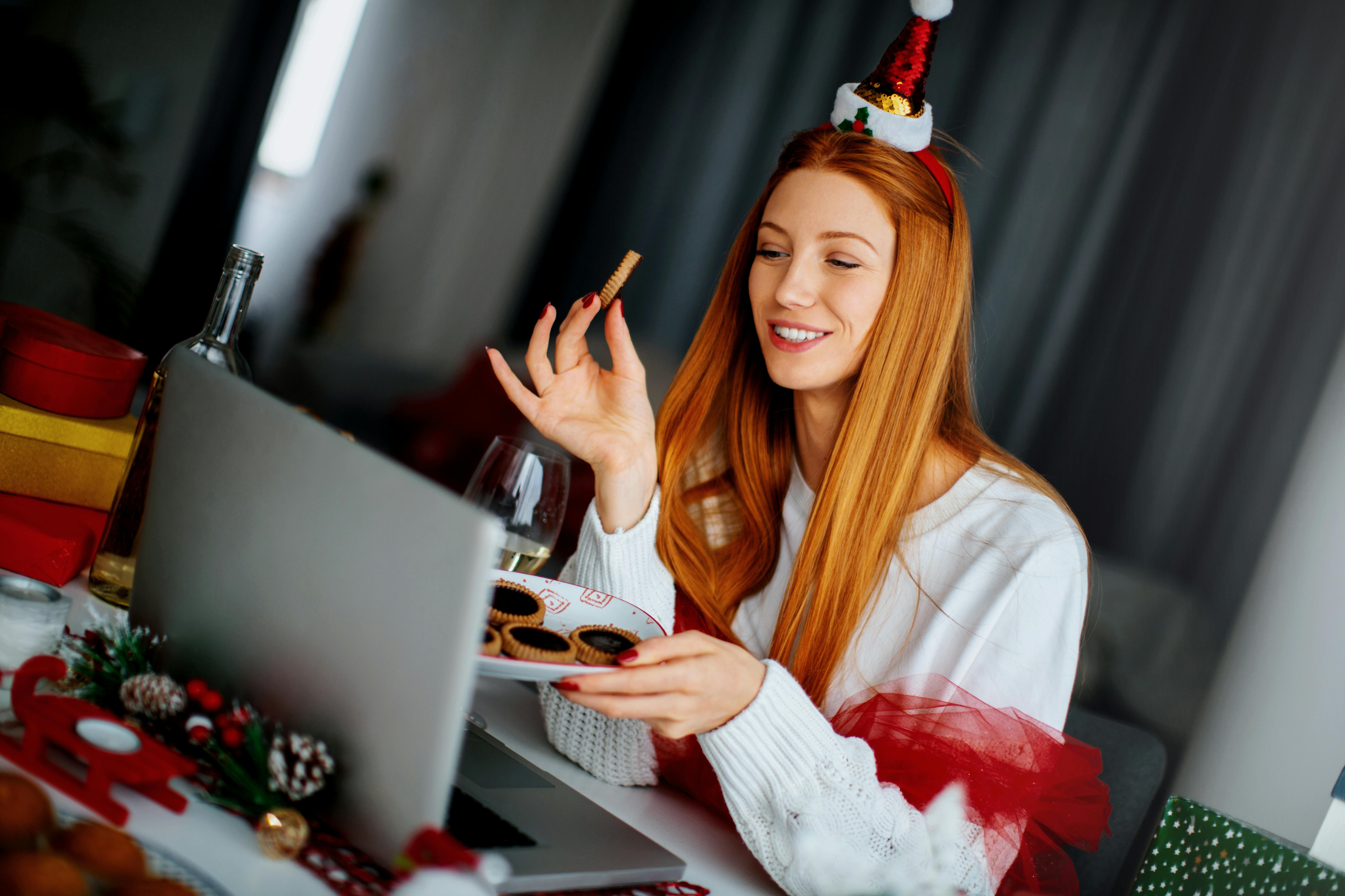 En julefrokost betyder masser af mad – og en virtuel julefrokost er ingen undtagelse! Kvinde spiser snacks foran computer.