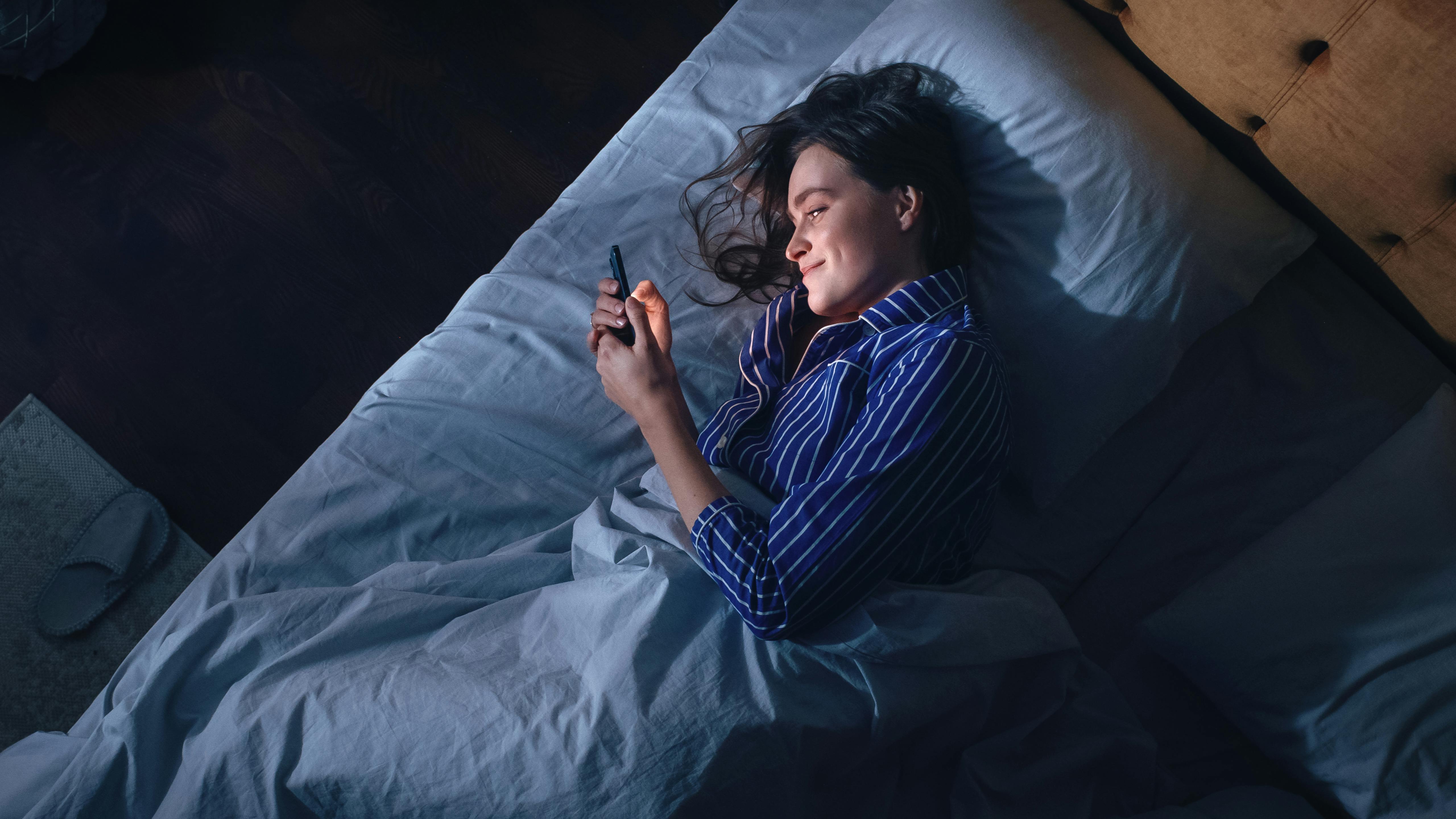 Øvelser gør mester – og telefonsex er ingen undtagelse. Kvinde i seng kigger i telefon efter telefonsex