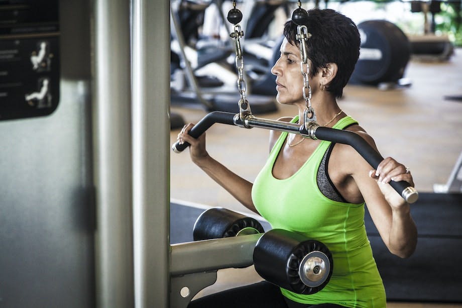 Pulldown Kvinna i grön överdel gör pull downs med överhandsgrepp