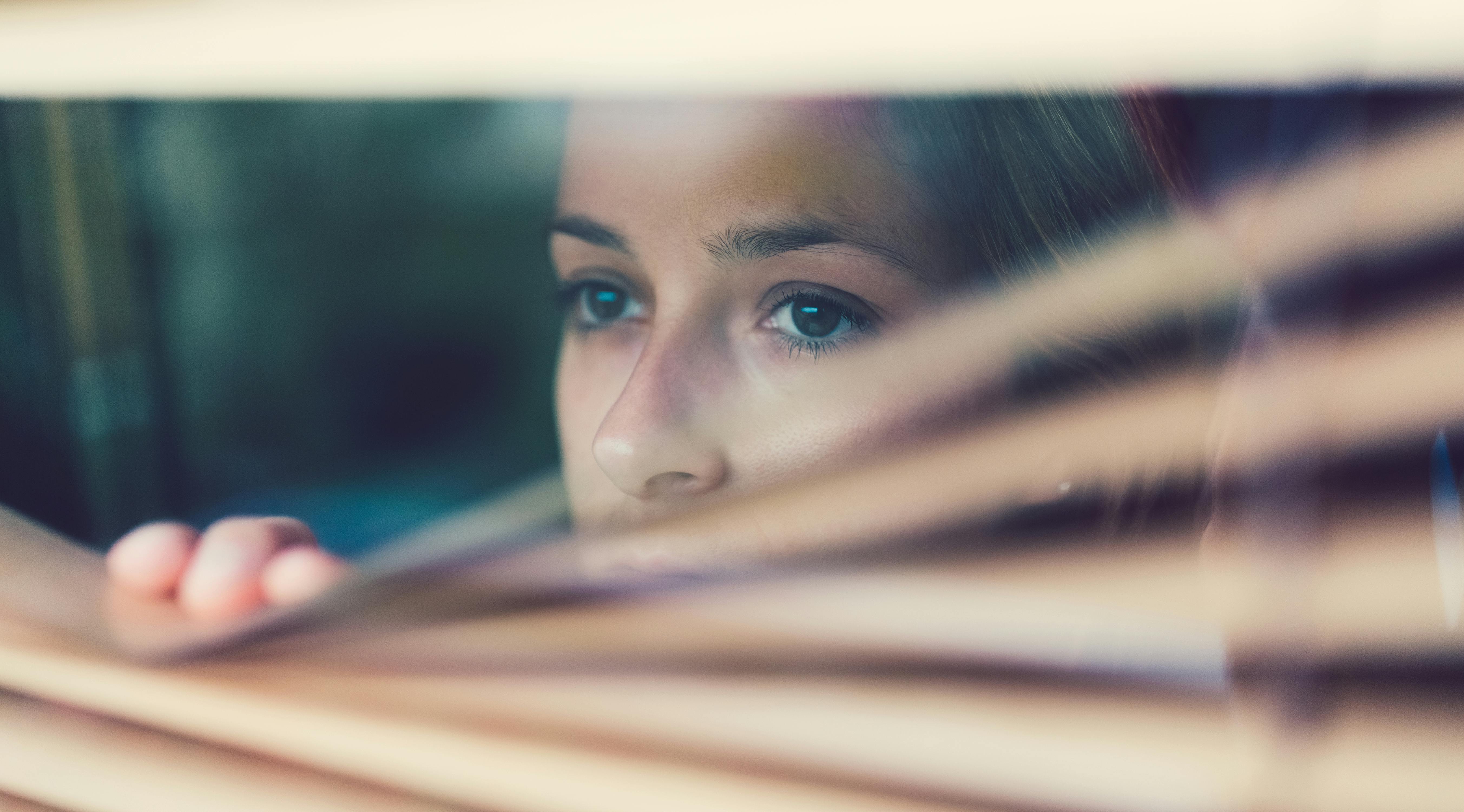 Den, der er ramt af OCD, føler ofte skam over sin lidelse. Kvinde kigger ud ad vindue med persienner