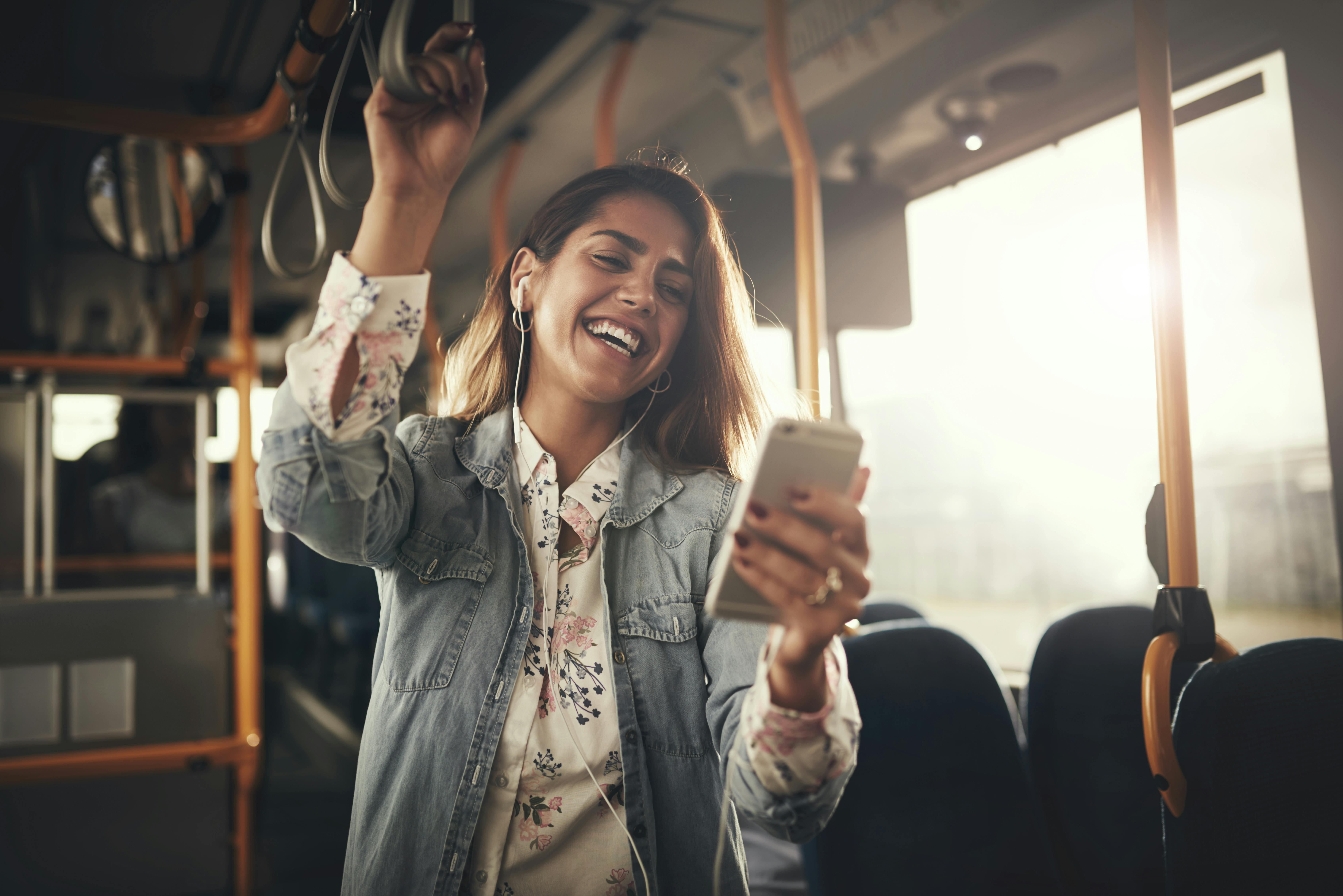 Det er nu ikke helt værst at være single – hvis vi selv skal sige det! Glad kvinde på mobilen i en bus