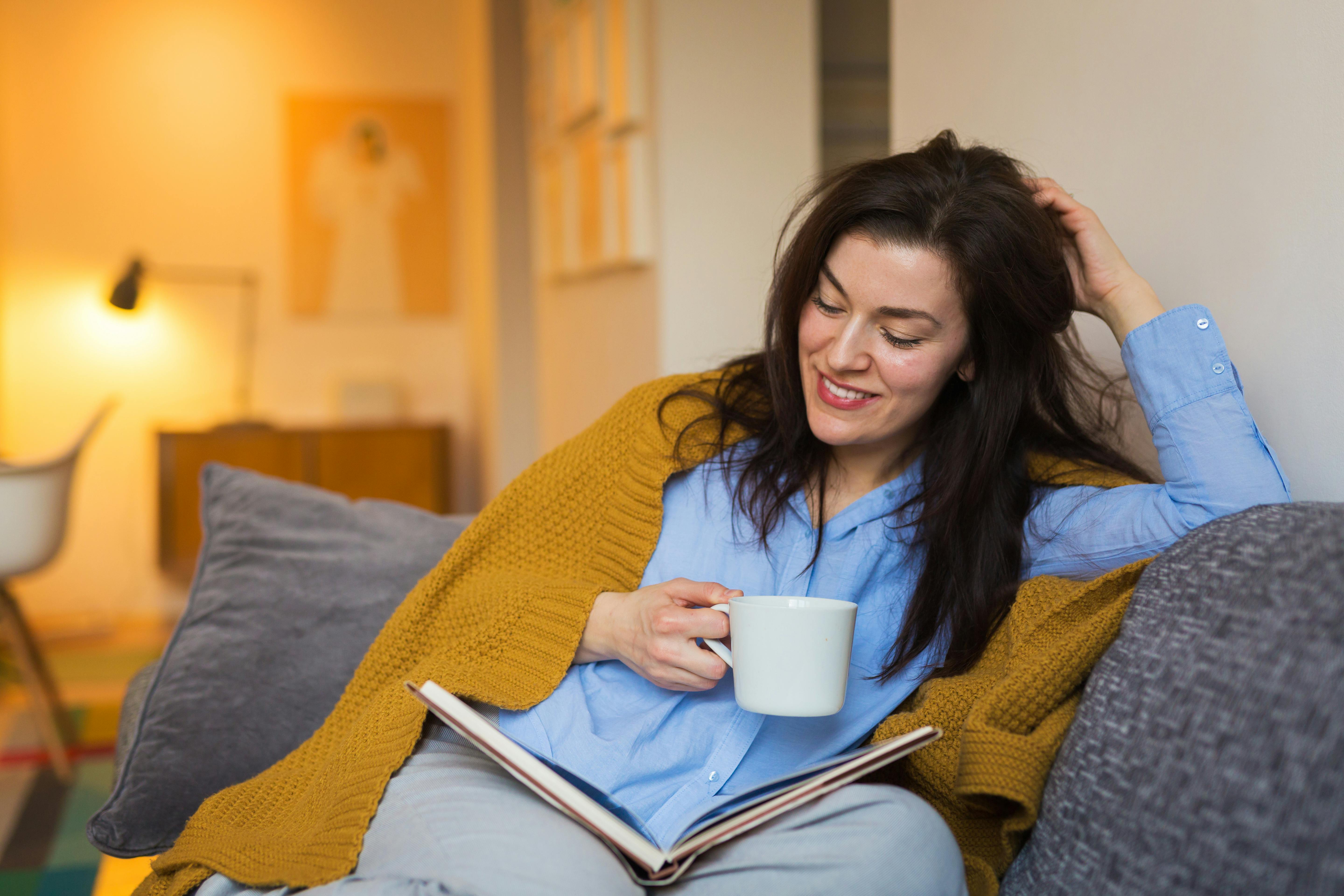 Fordyb dig i en god roman og glem omverdenen. Kvinde læser roman og drikker kaffe i sofa