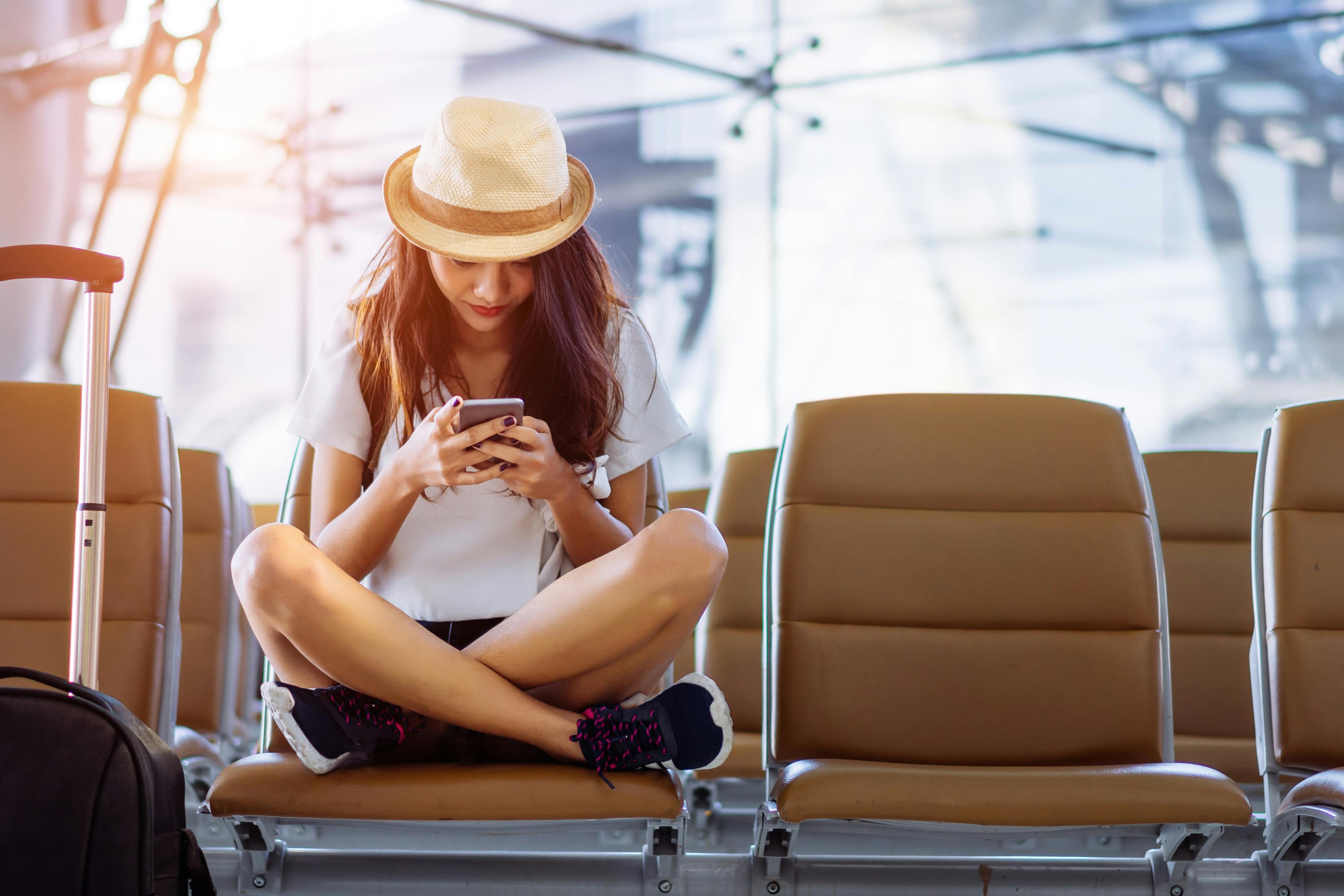 Du kan bruge tiden i lufthavnen til at planlægge din tur med dine rejseapps. Kvinde i lufthavn med telefon