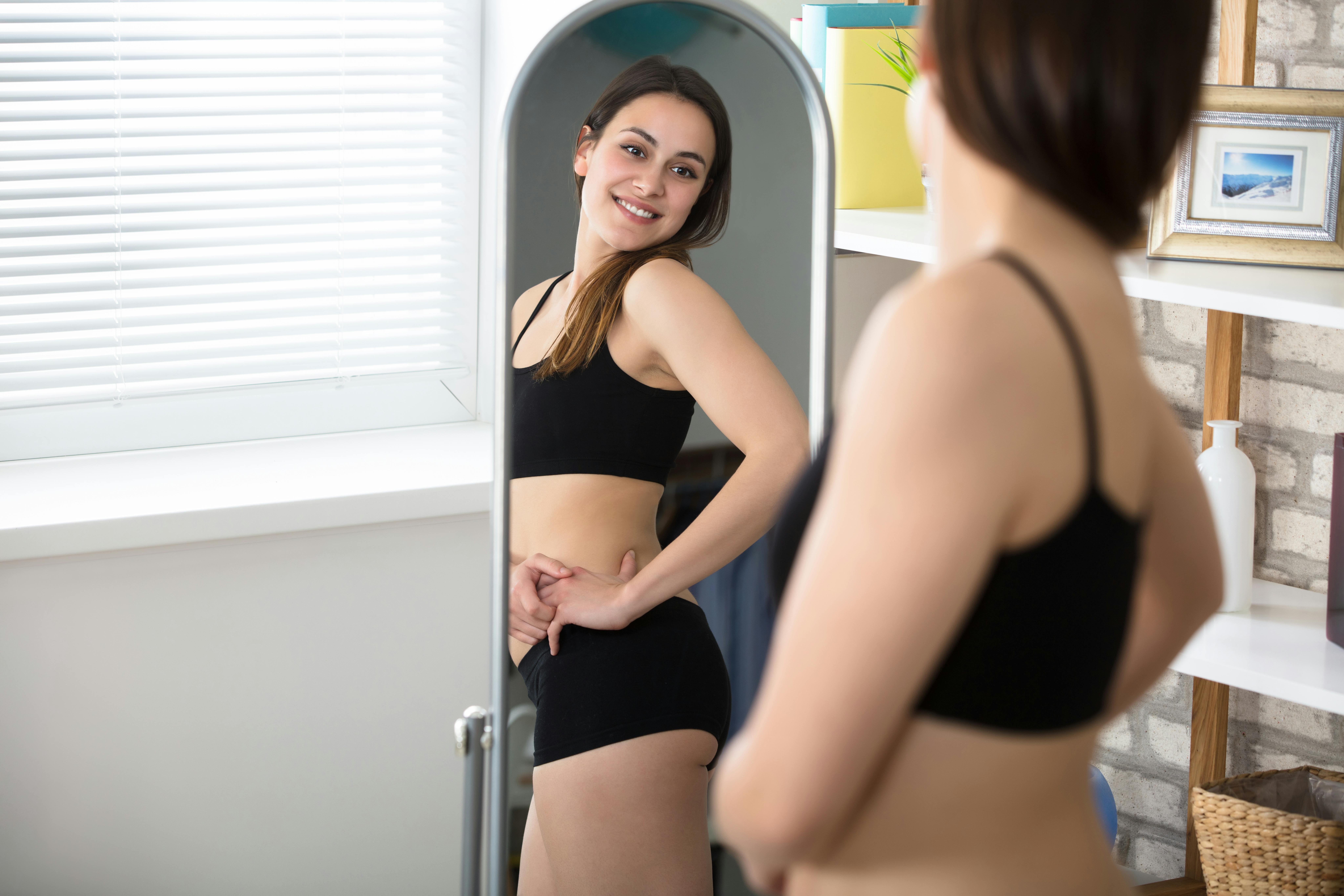 Du er virkelig smuk, som du er – sig det til dig selv og tro på det! en glad smilende kvinde kigger på sit spejlbillede
