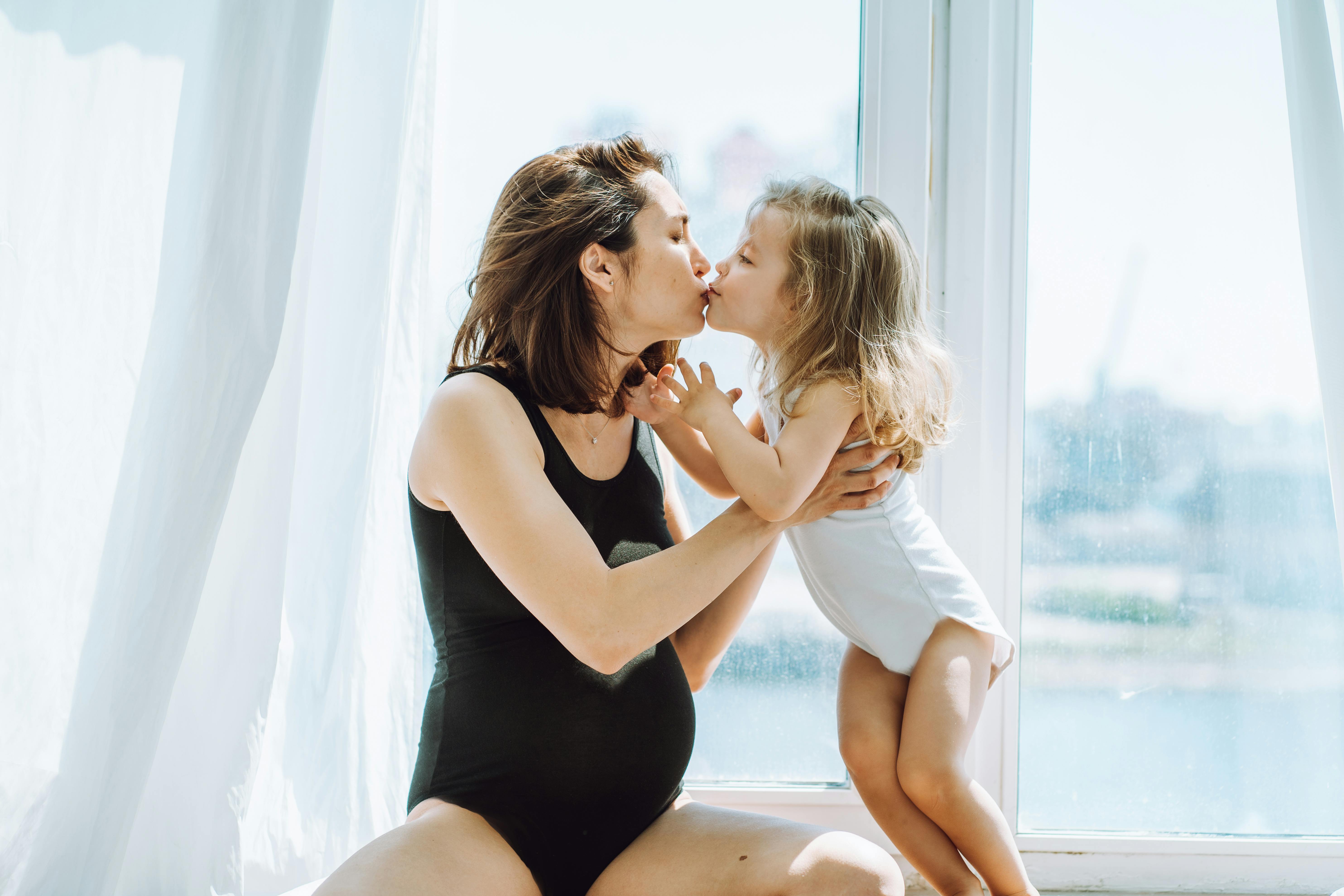 I uge 20 af graviditeten er du nået halvvejs igennem. Kvinde, der er gravid i uge 20, kysser sit barn