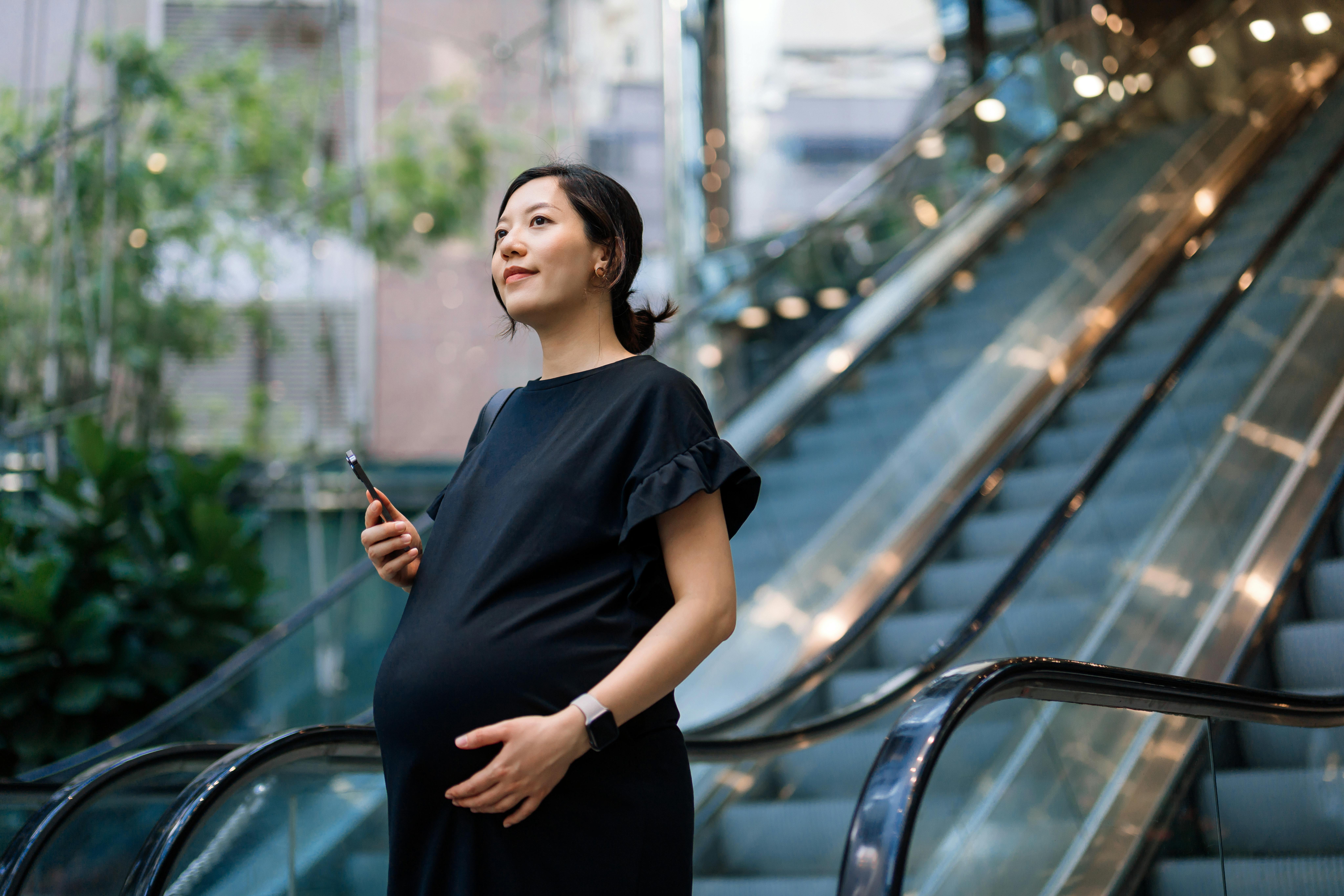 Uge 27 af din graviditet er den sidste i andet trimester. Kvinde, som er gravid i uge 27, står foran bygninger og rulletrappe