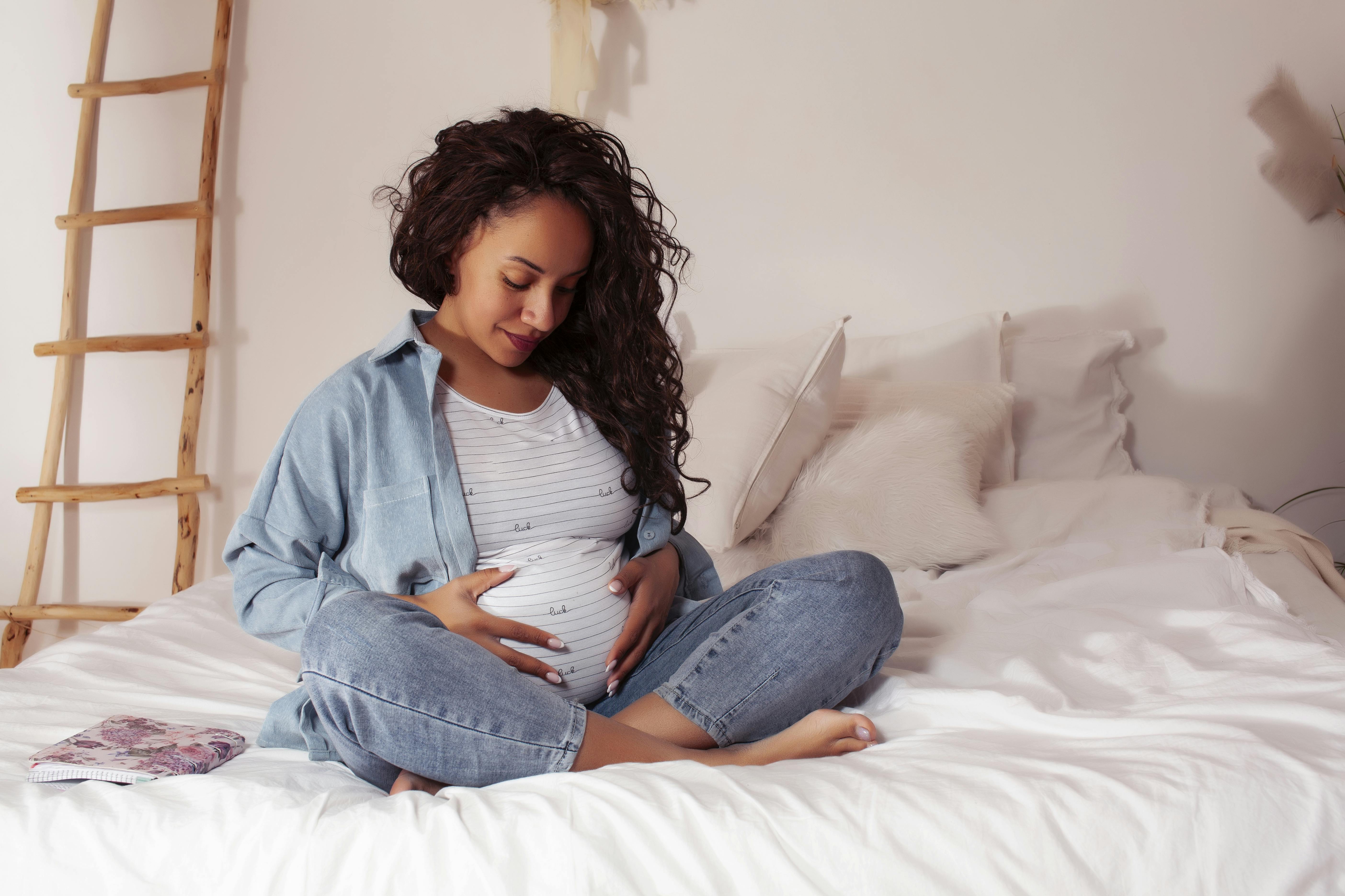 Du får måske mere tissetrang og mindre appetit som gravid i uge 19. Kvinde, der er gravid i uge 19, sidder i en seng og rører sin mave