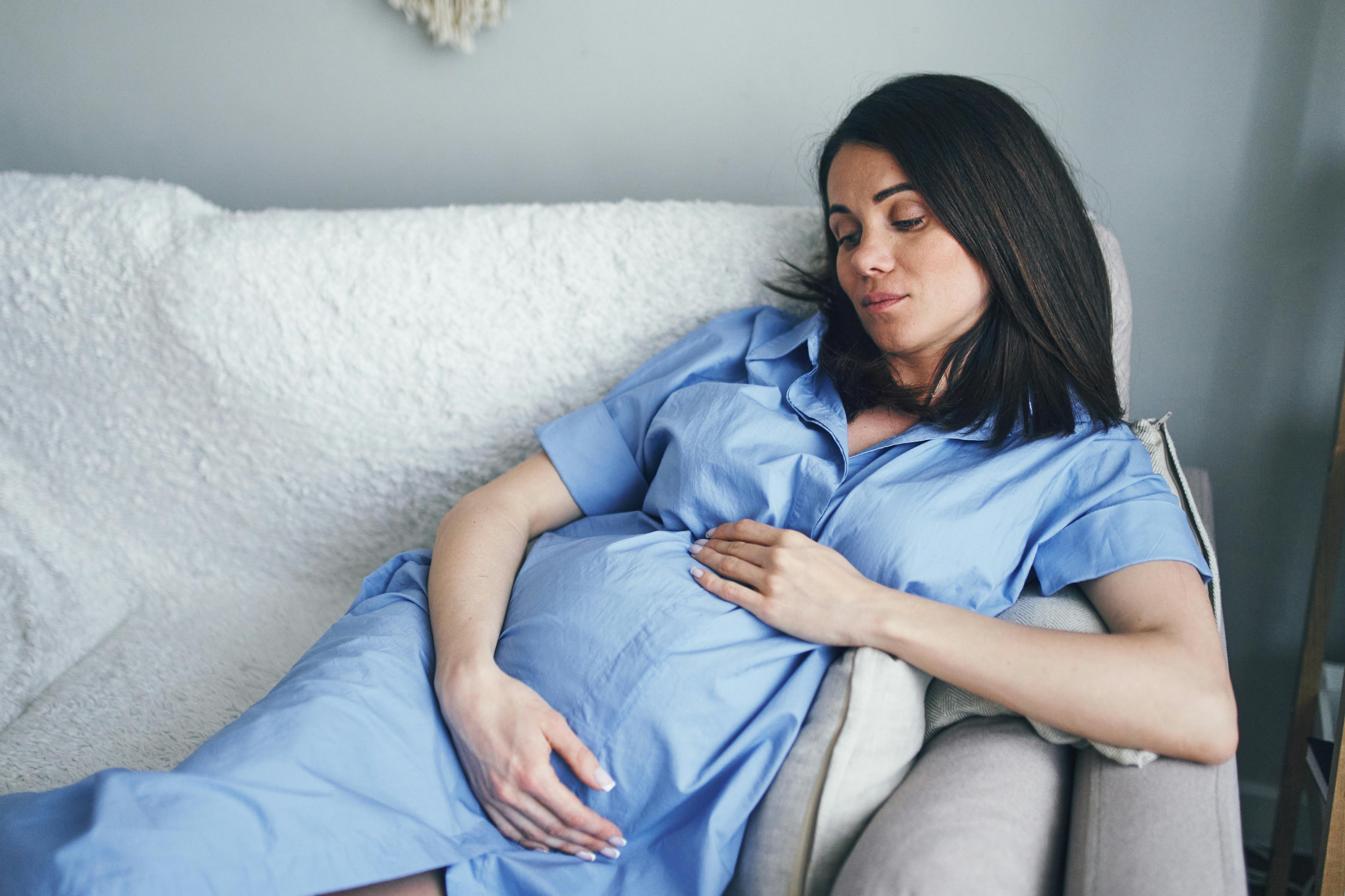 Hvis det er svært at ligge på ryggen som gravid i uge 29, kan du prøve at ligge på siden. Kvinde, som er gravid i uge 29, ligger på sofaen