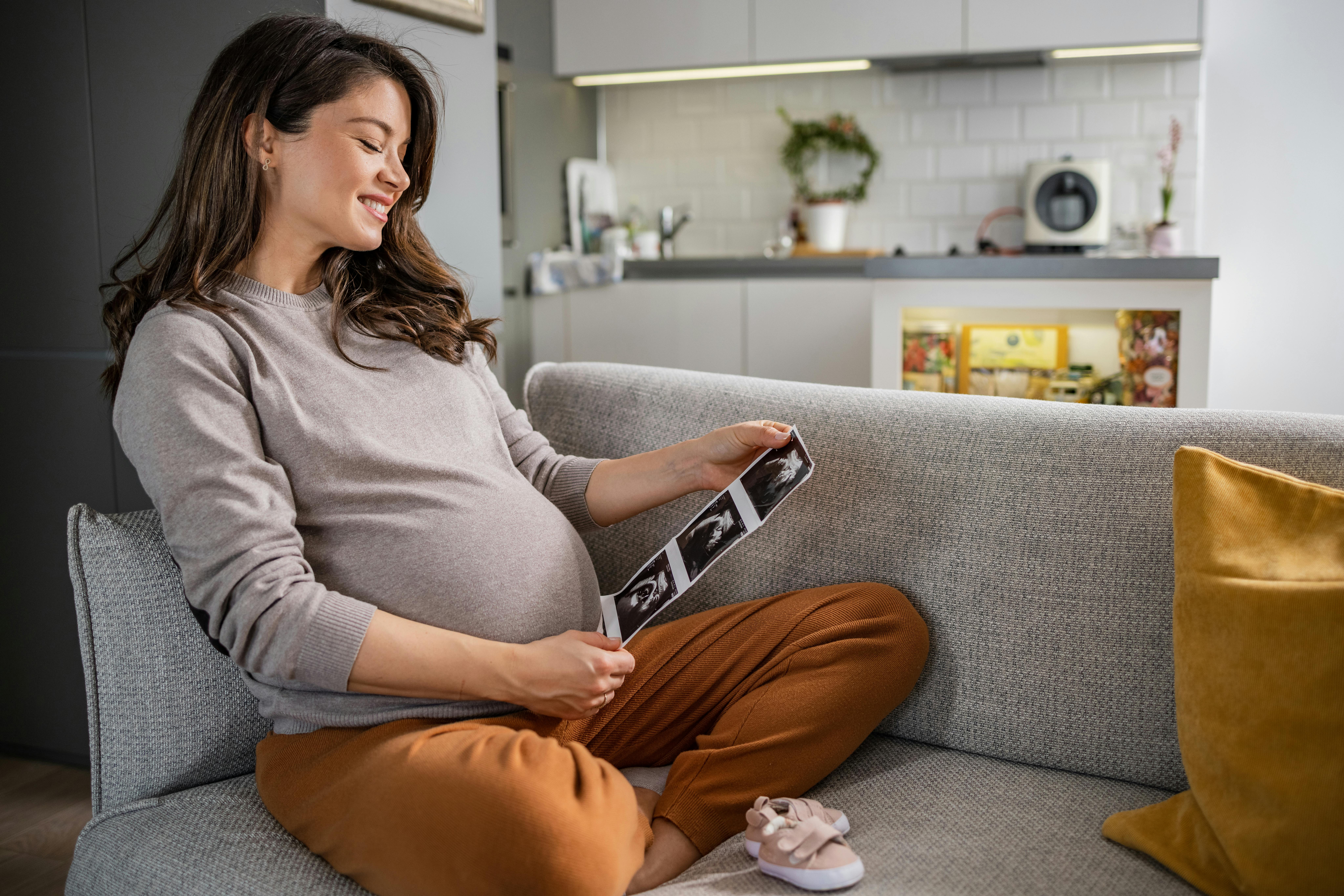 Inde i maven vejer dit foster knapt to kilo, når du er gravid i uge 32. Kvinde, som er gravid i uge 32, ser på skanningsbilleder af sin baby i sofaen