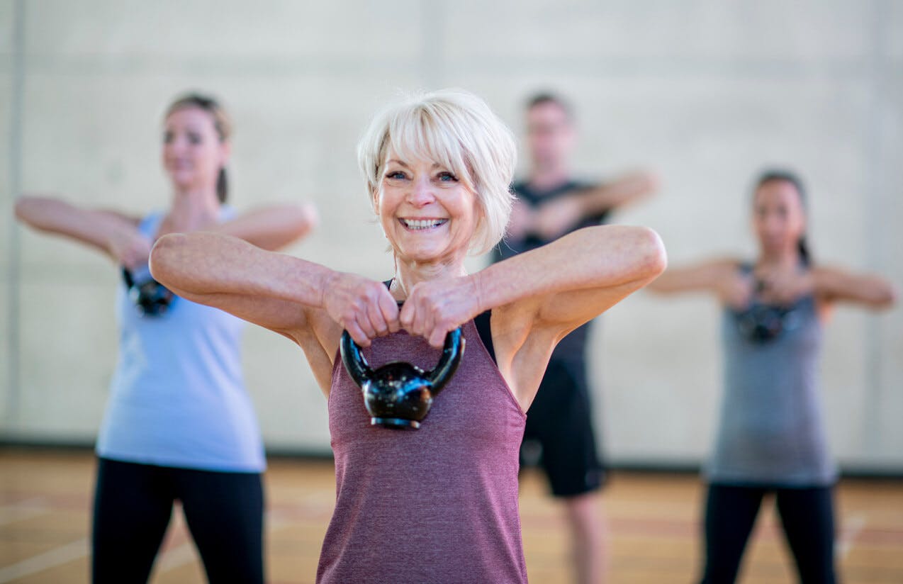 Styrketræning er især vigtig, når du har rundet de 40 år. midlaldrende smilende kvinde løfter kettlebell