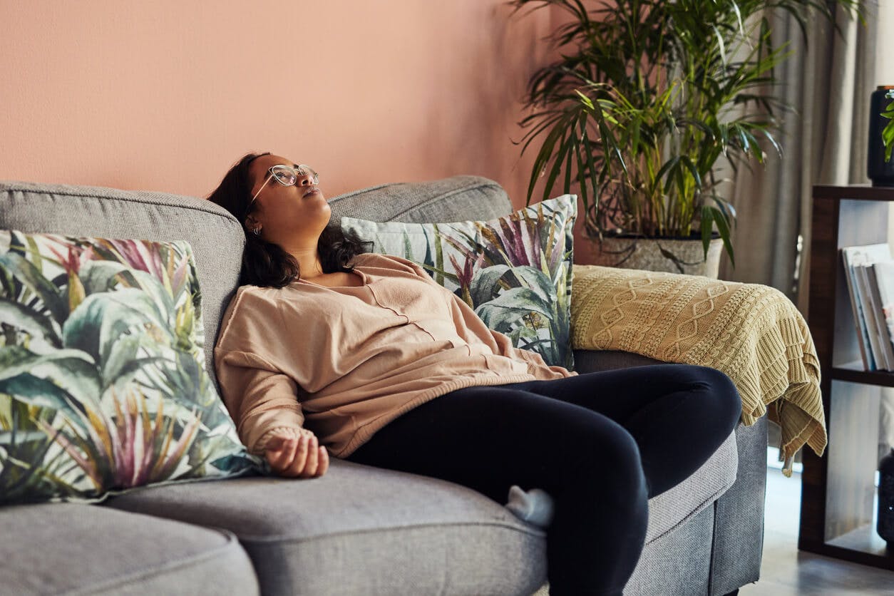 Det kan være svært at nå de 7-8 timers anbefalede søvn i døgnet. Træt yngre kvinde sidder lænet tilbage i sofa
