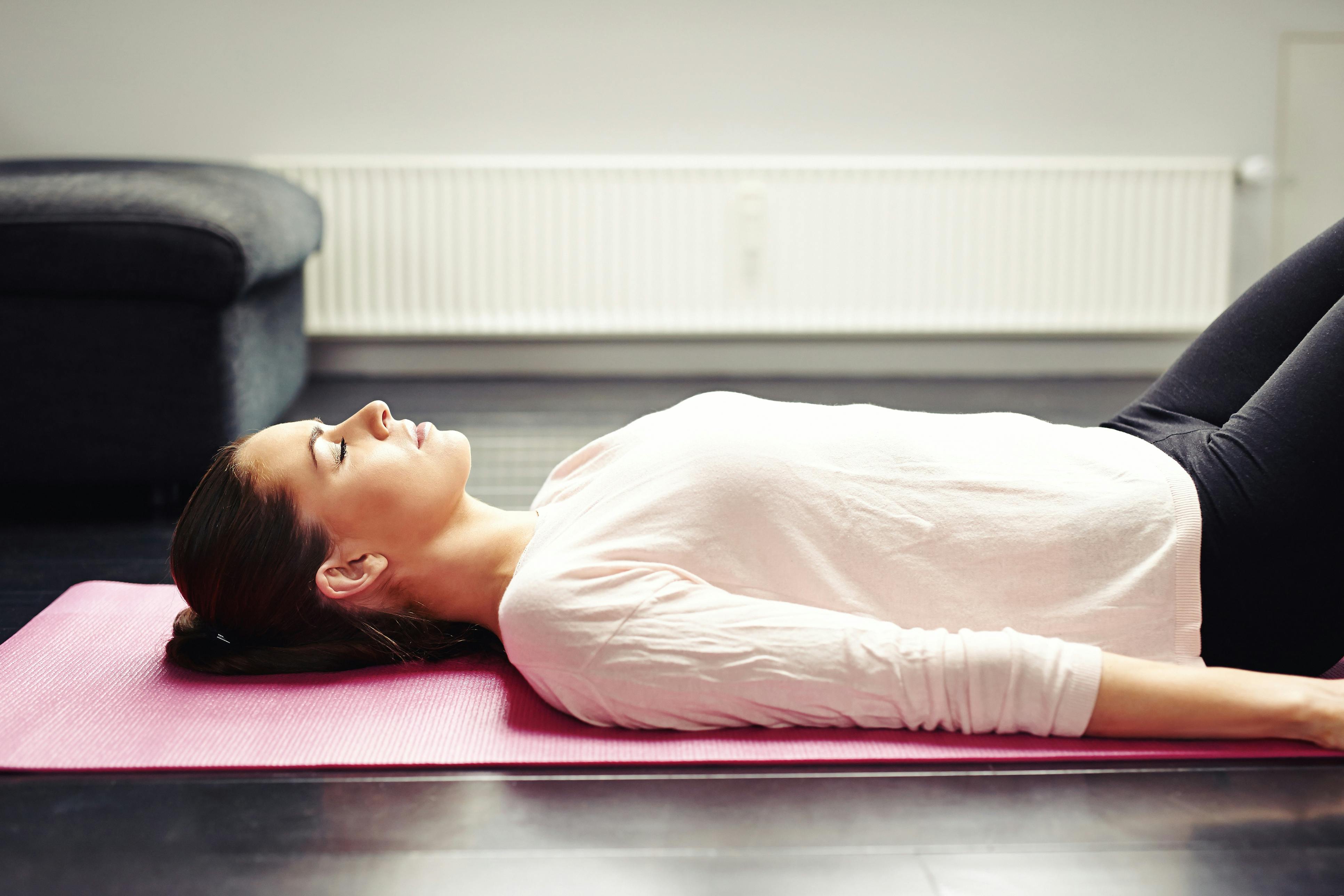 Kvinde ligger på yogamåtte med lukkede øjne