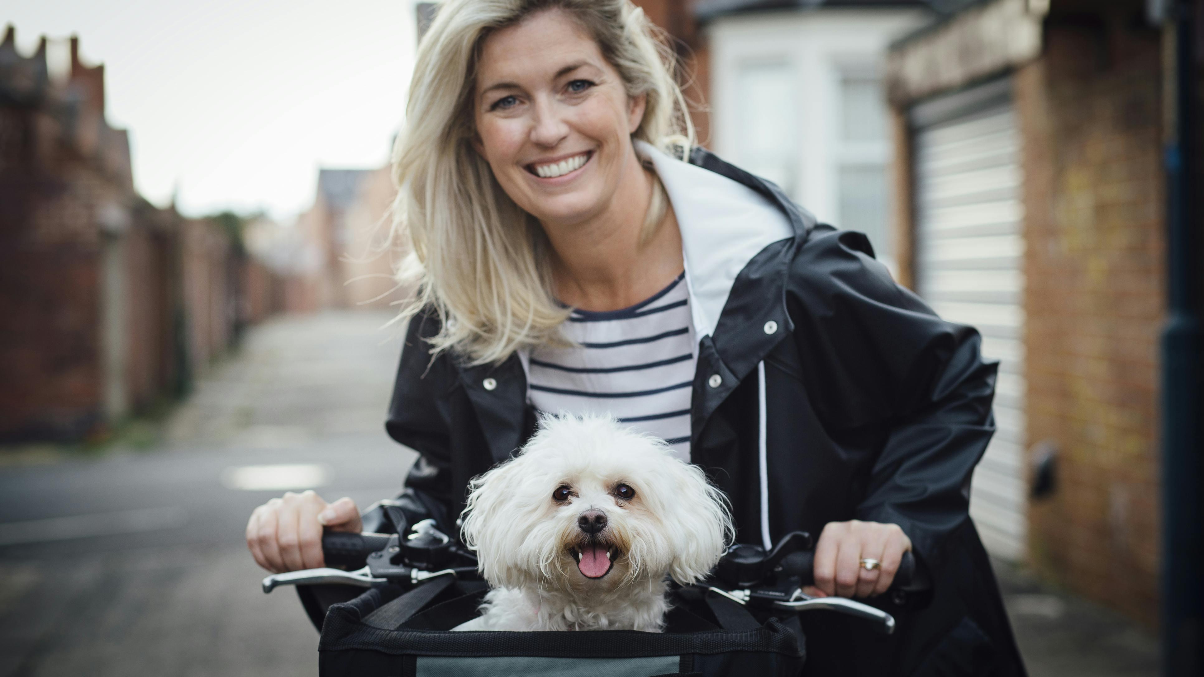 Kvinde i regnjakke har sin lille hund i cykelkurven