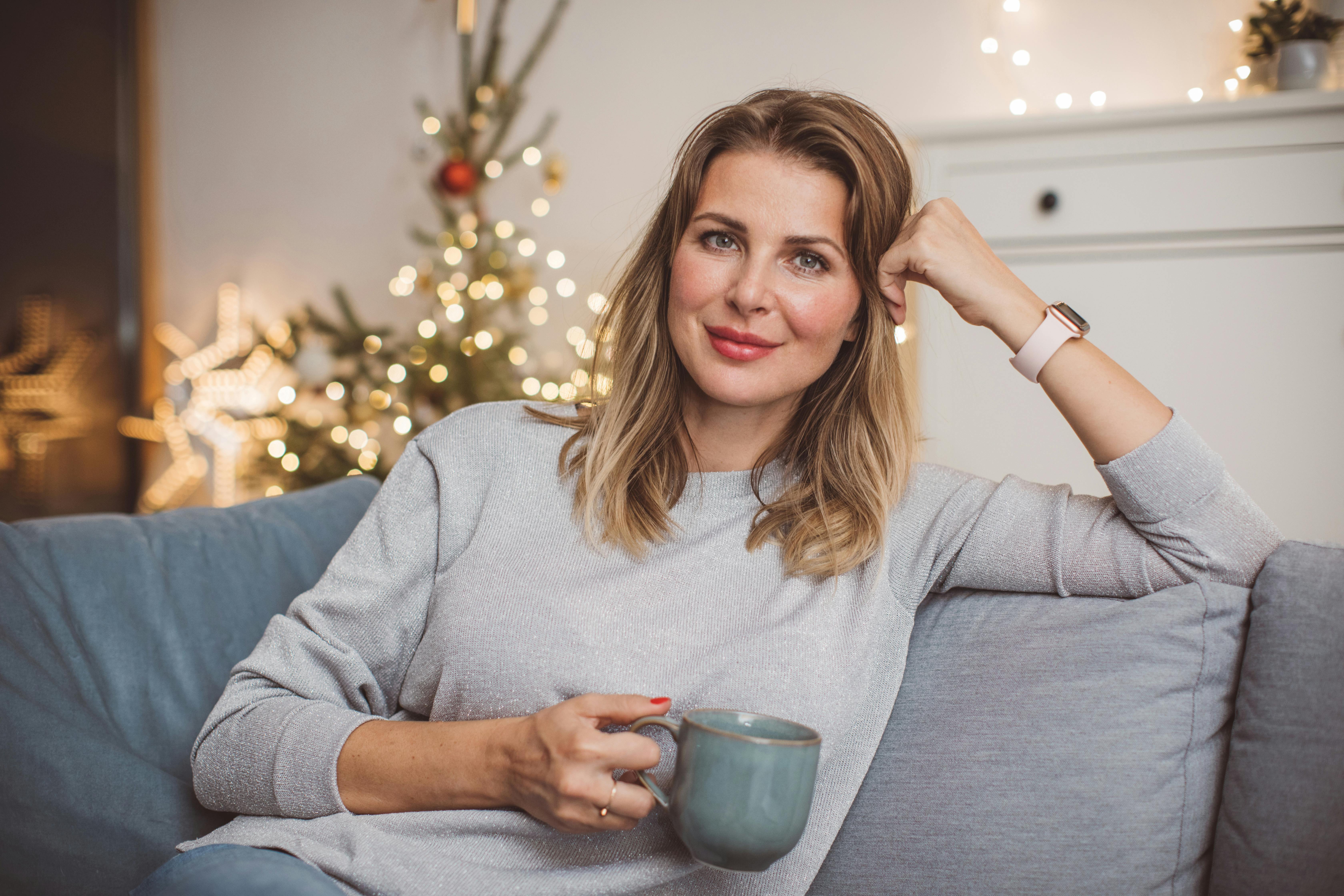 Singlejul, skilsmissejul, delejul. Del de svære julefølelser med dem, du fejrer jul med. Moden kvinde drikker kaffe og sidder i en sofa til jul