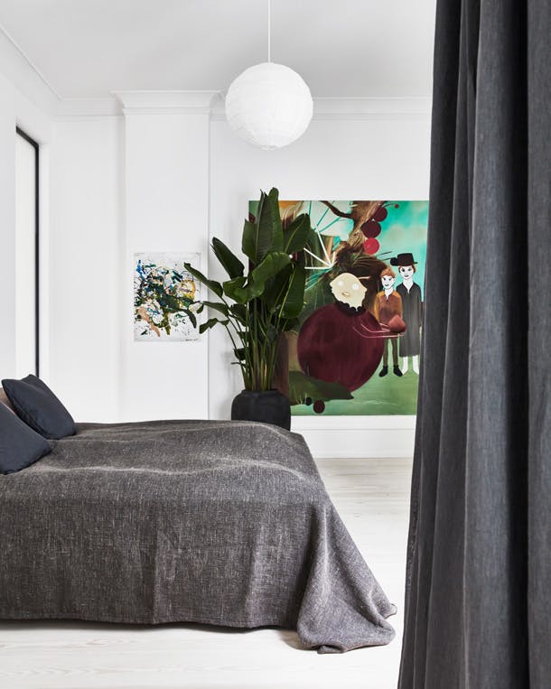 Een grote plant en kleurrijk schilderij geven diepte aan de lichte slaapkamer. Luxe slaapkamer met grote plant en groot schilderij