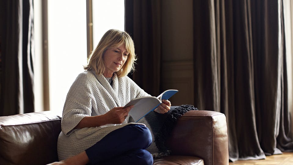 Smæk benene op mens kulden raser udenfor. Moden kvinde sidder og læser i sofaen