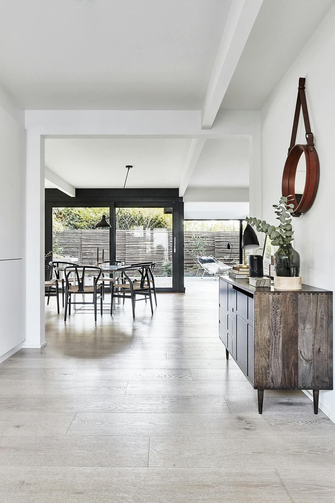 De zichtbare constructie in het plafond verbindt de entree met de aangrenzende ruimtes. Het dressoir is van Mater, de spiegel met leer van Gubi is in de jaren 1950 ontworpen door Jacques Adnet. Dressoir van Mater, spiegel van Gubi.