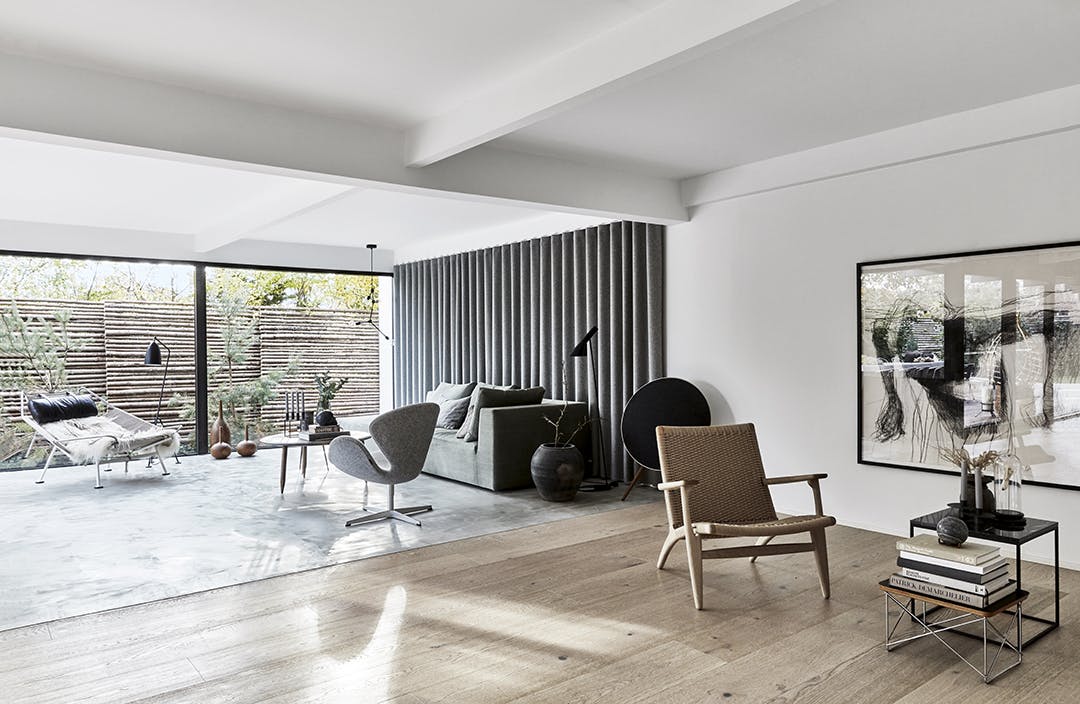 Twee vloeren, een gietvloer en een houten vloer, vinden elkaar halverwege de open ruimte. Woonkamer met gegoten betonvloer. parket en Scandic design meubels.