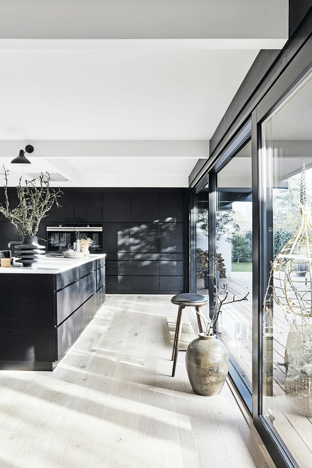 Het kookeiland van zwartgebeitst hout is van Kvik. De barkruk is een ontwerp van Space Copenhagen voor Mater en de vaas komt van Atelier du Noir. De lamp is een Mantis, ontworpen door Bernard Schottlander. Minimalistische zwarte keuken met kookeiland en barkruk.
