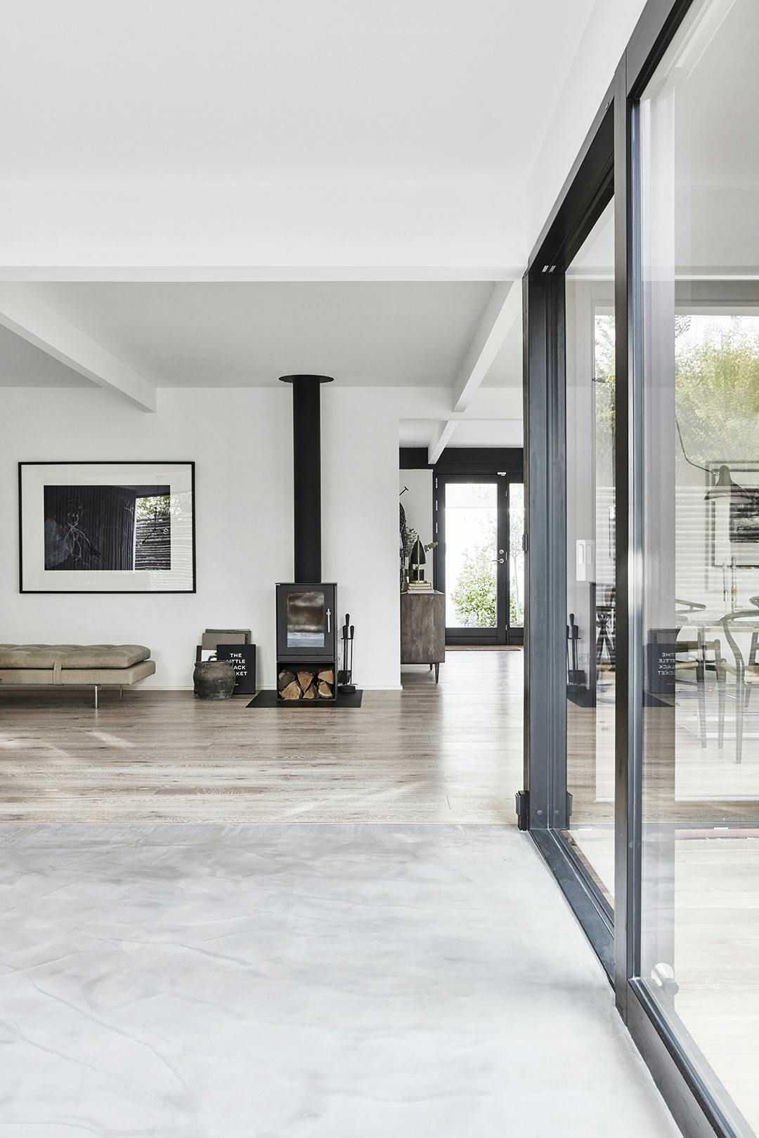 Vanuit de woonkamer loop je zo het terras op door de grote glazen schuifpuien, die ook het buiten en binnenleven tot een eenheid maken. Woonkamer met gegoten beton vloer en parket, en zwarte houtkachel.
