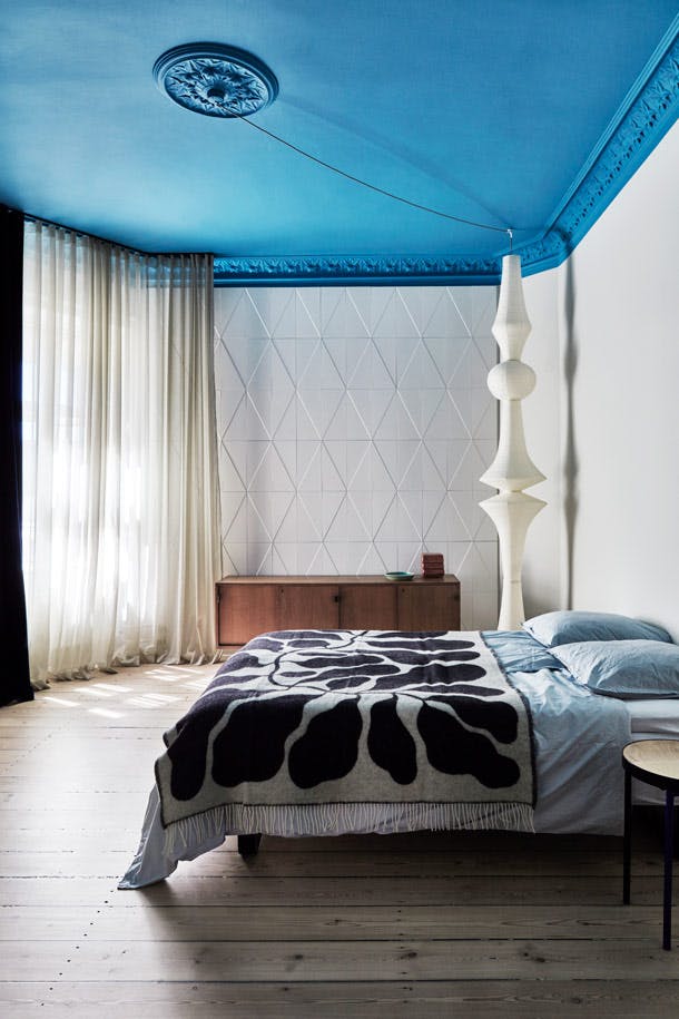 de kleuren in de slaapkamer zijn koel, en het blauwe plafond geeft het gevoel dat je onder de hemel wakker wordt. De enige decoratieve elementen zijn de grafische tegels van H+O en de ingenieuze lamp Akari van rijstpapier. Slaapkamer met geverfd plafond en transparante gordijnen