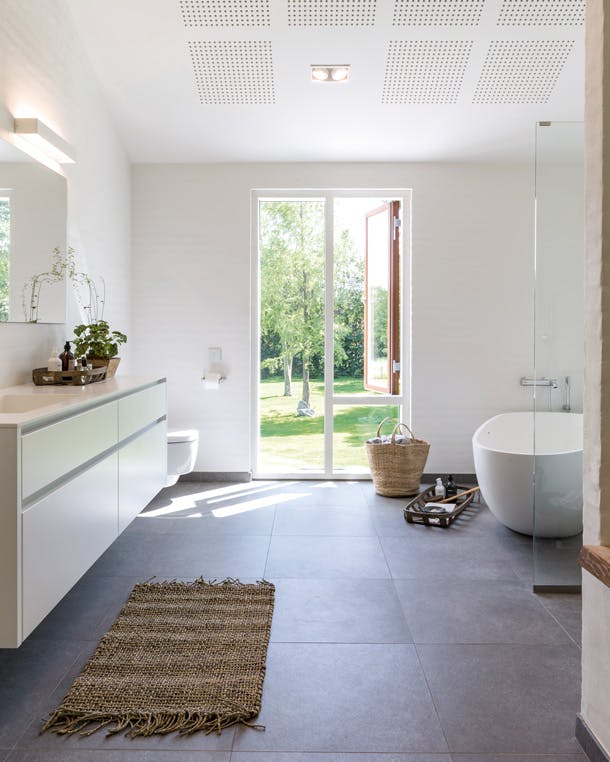 De ruime badkamer kijkt uit op het oude erf. lichte badkamer met donkere tegelvloer en vrijstaand bad