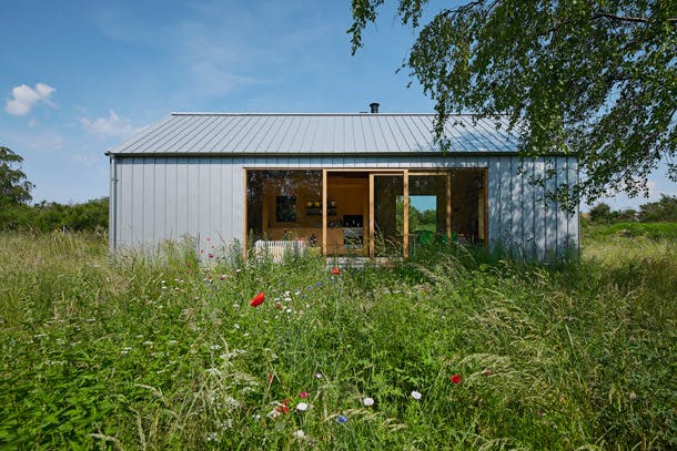 Als een doos van metaal en hout staat het eenvoudige vakantiehuis midden in de weelderige natuur, wat een contrastrijk geheel vormt. Stalen design vakantiehuis in de natuur met klaprozen