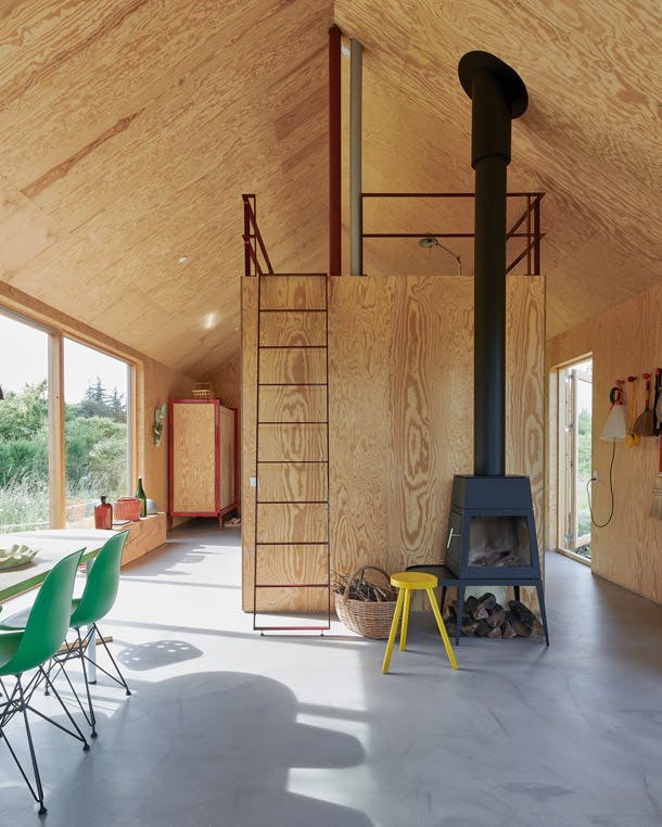 Binnen is multiplex het bepalende materiaal. In de winter wordt het uitstekend geïsoleerde huis uitsluitend verwarmd door de houtkachel Shaker van Antonio Citterio voor Skantherm. houten woning met betonnen gietvloer en vliering