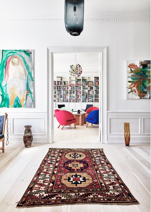 Klassieke Perzische tapijten worden afgewisseld met moderne kunst. In de achtergrond zien we een kwartet van Pelican-stoelen van Finn Juhl. licht scandinavische woonkamer met moderne kunst en perzisch tapijt