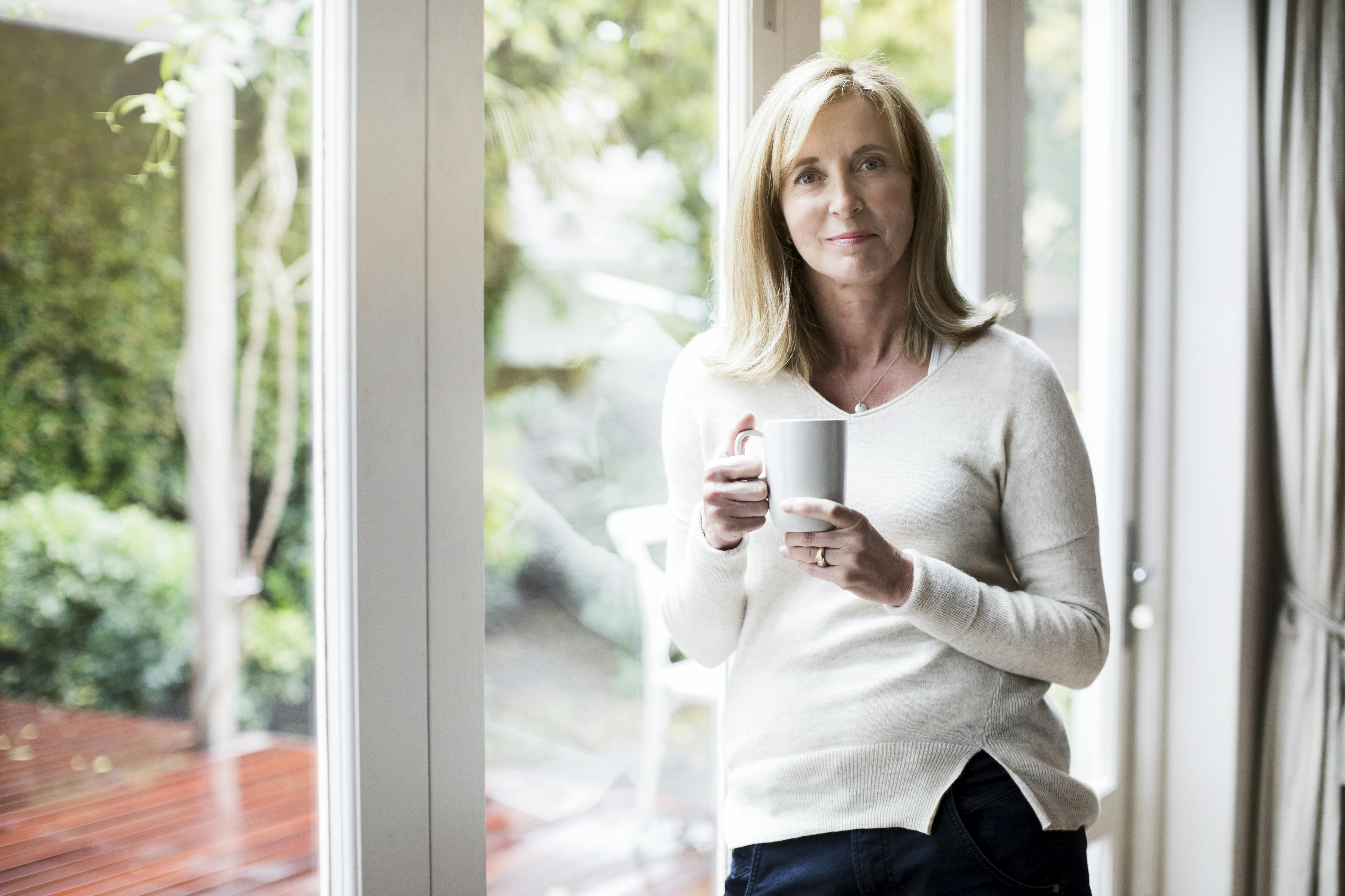 Indfør en eller flere pauser, hvor du konkret slukker mobilen og laver noget andet. Moden kvinde drikker kaffe eller te ved vinduet