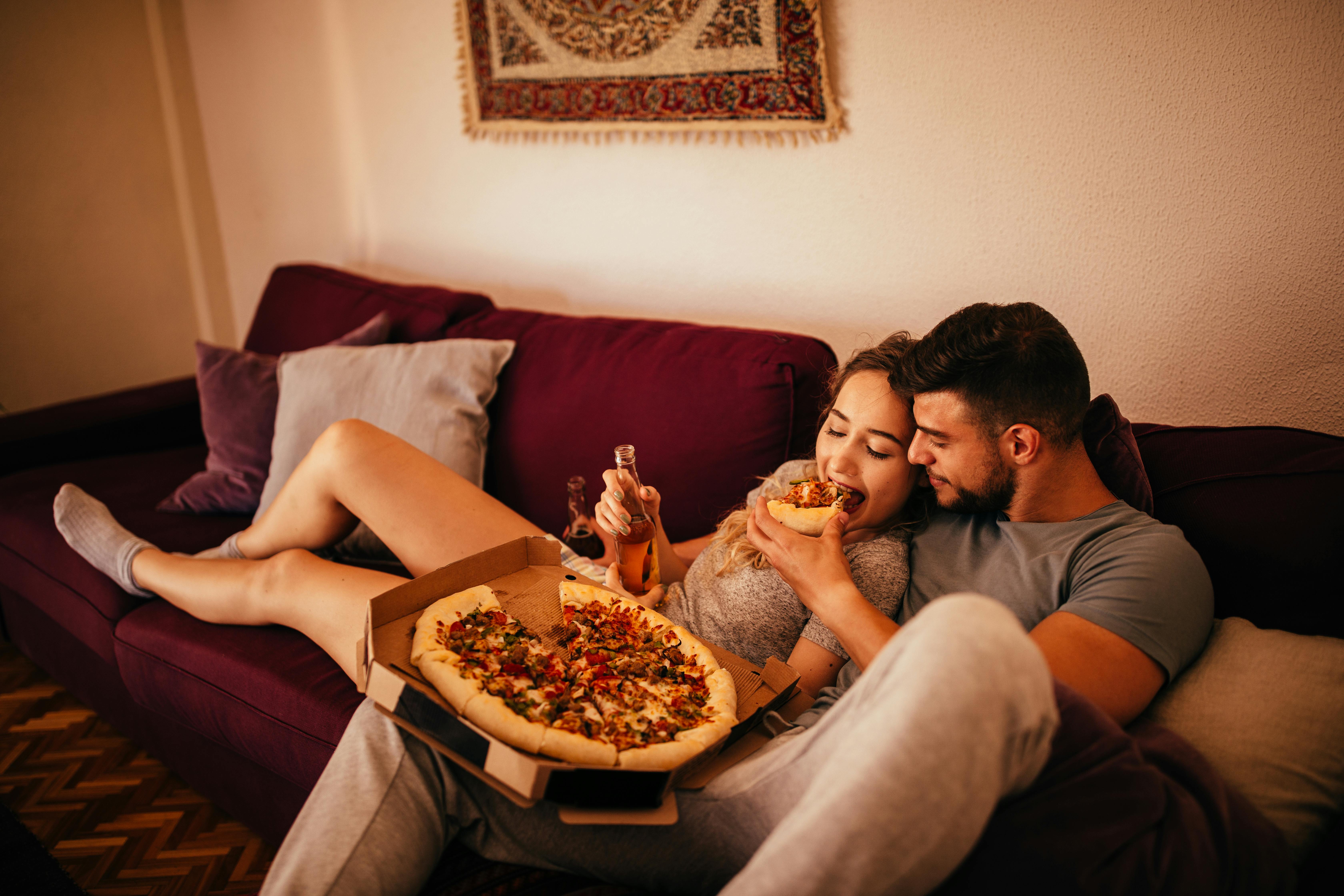 Vælg en dag, hvor I skal se film hele dagen! Kvinde og mand på sofa spiser pizza