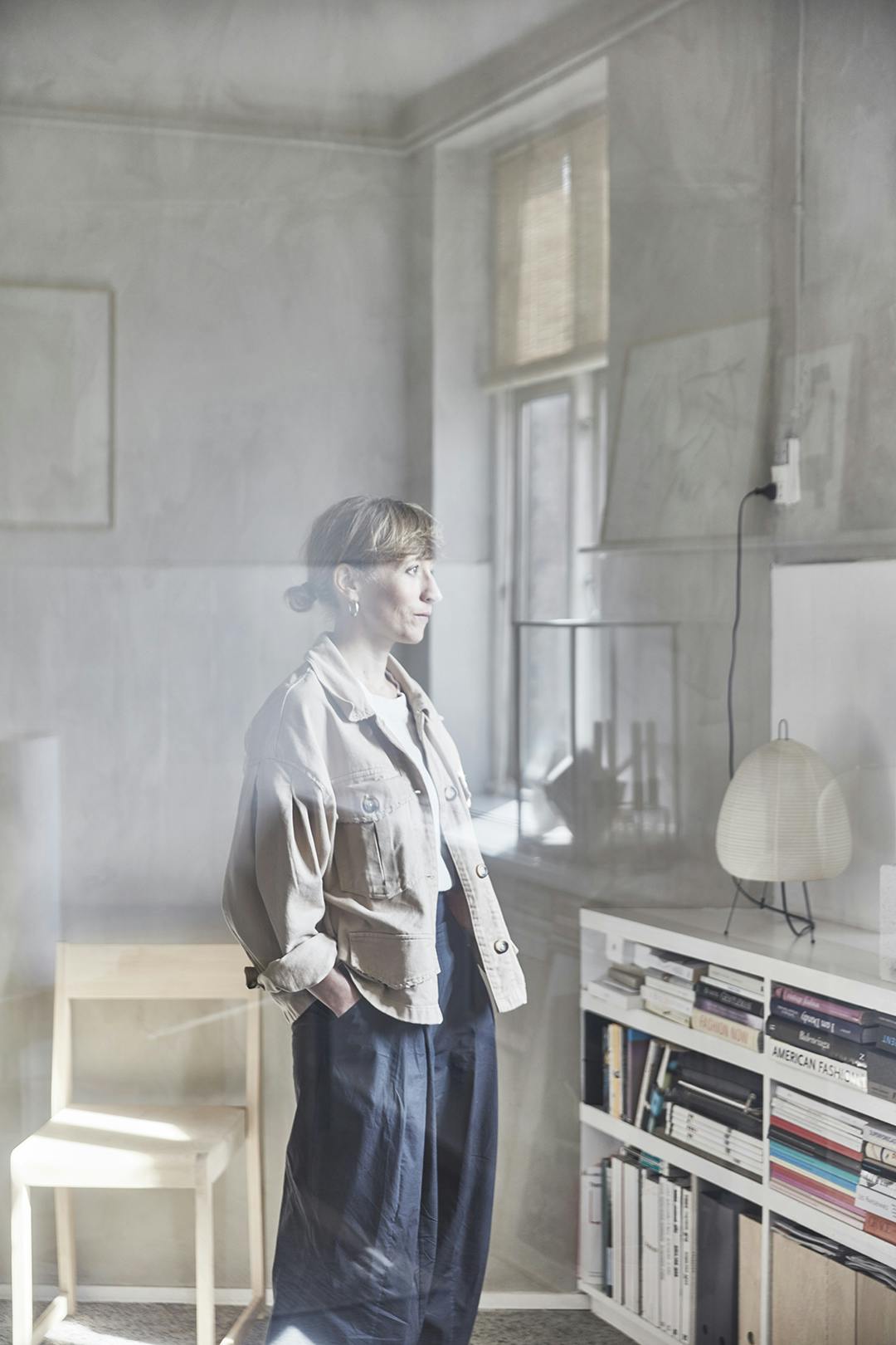 Sara kijkt uit het raam van de Atelier Cph studio. Aan de andere kant van het grote binnenraam, waar de fotograaf staat, zijn Sara’s woonkamer en keuken. Zo is de grens tussen werk en privé transparant. Sara Ingemann in hybride Atelier Cph studio.