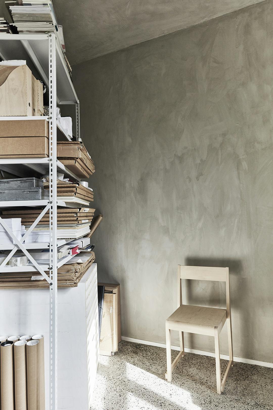 De onafgewerkte muur is een goed voorbeeld van de tactiliteit die Sara overal in huis aanbrengt. De stellingkast met prints geeft de plek het gevoel van een atelier. Atelier Cph studio met archiefkast, beige wand en granito.