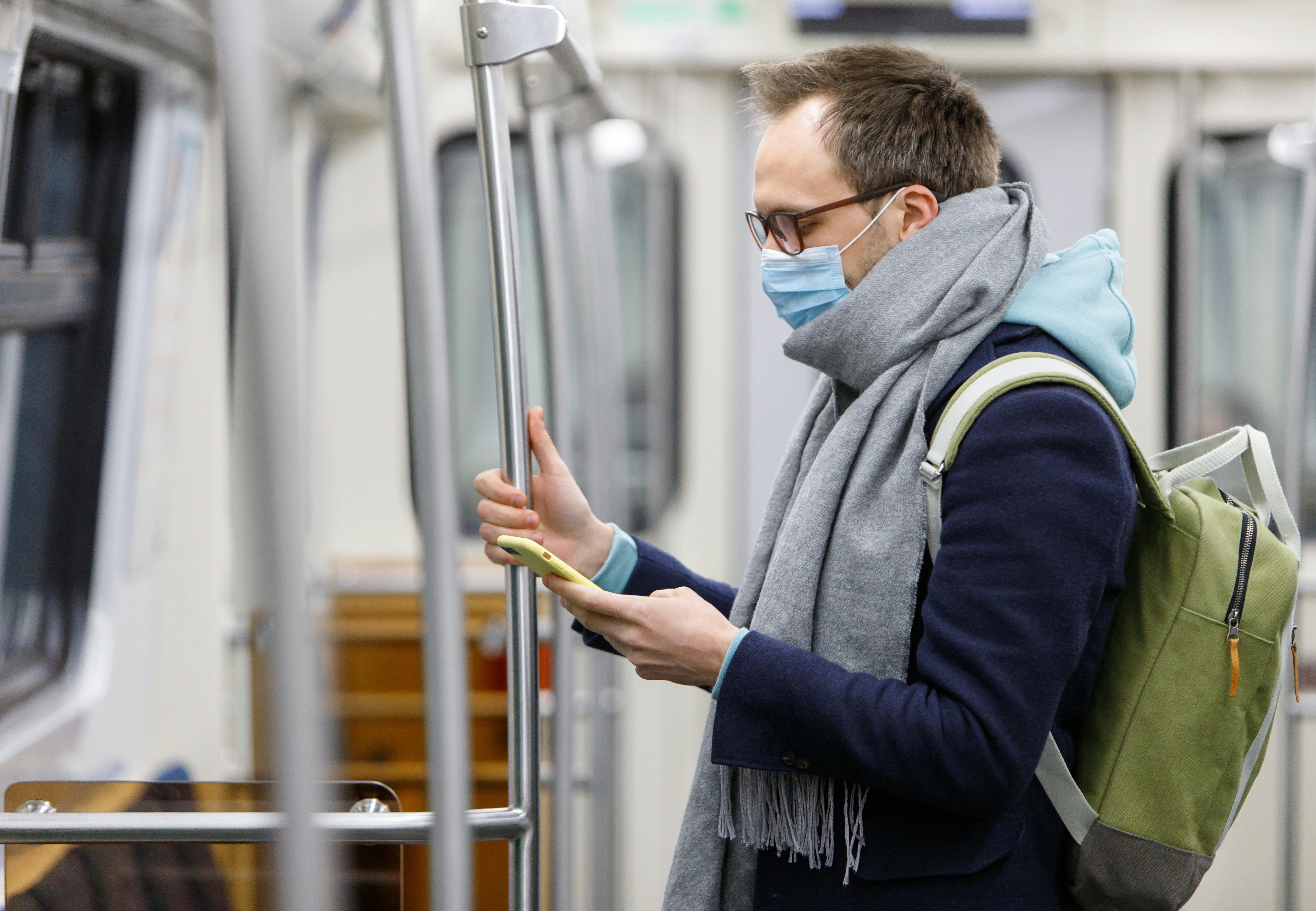 mand med hospitalsmaske kigger på sin smartphone imens har står i et tog